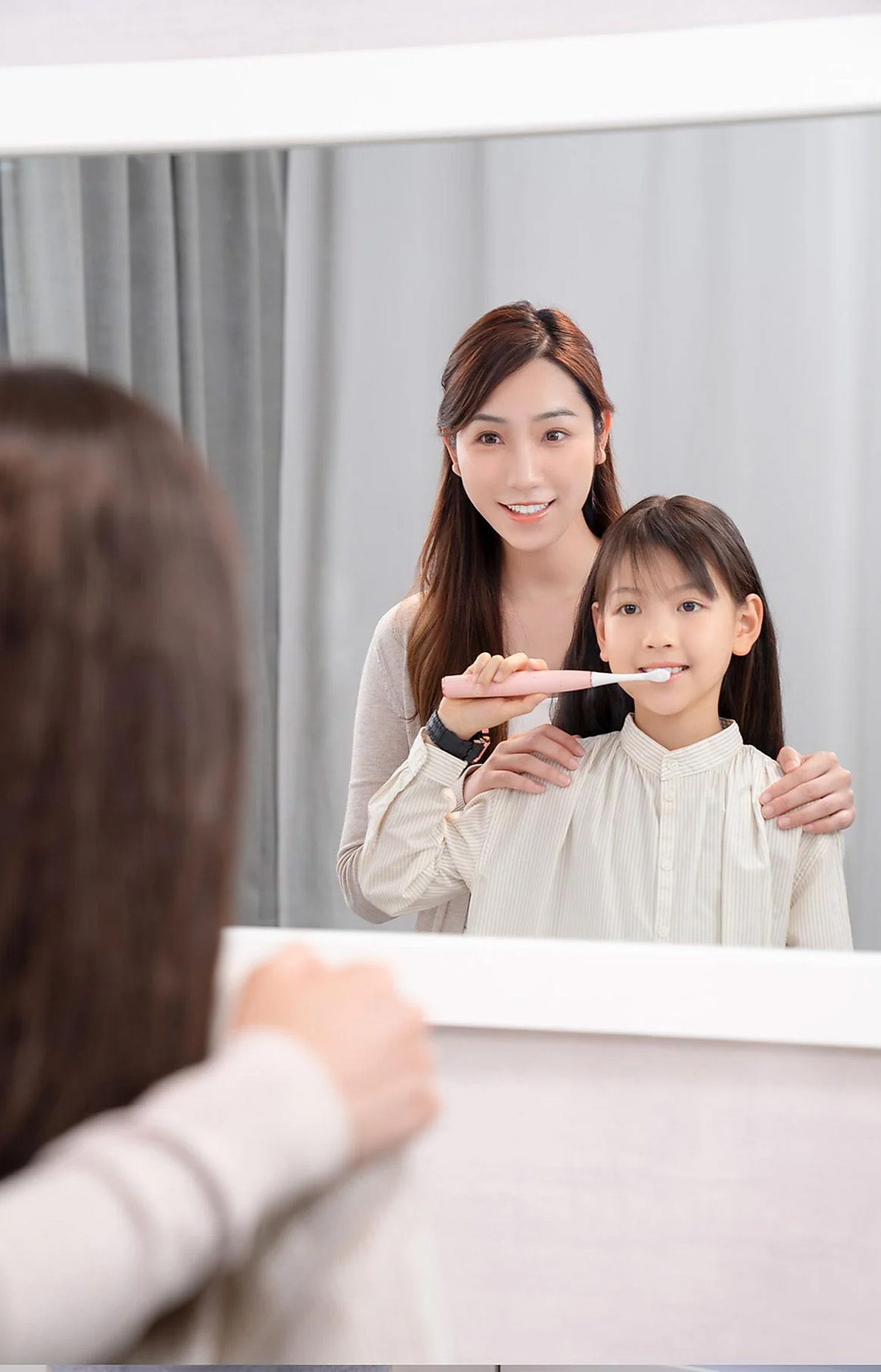 Matka i córka myją zęby przed lustrem. Córka szczotkuje.