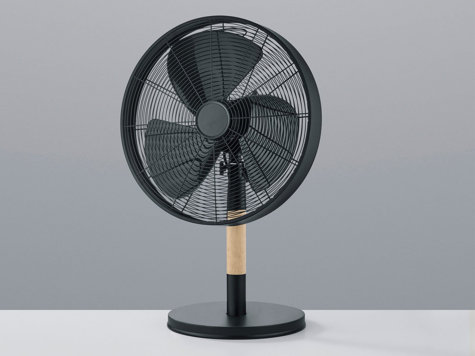 Ein schwarzer und holzfarbener elektrischer Ventilator auf weißer Oberfläche, grauer Hintergrund.