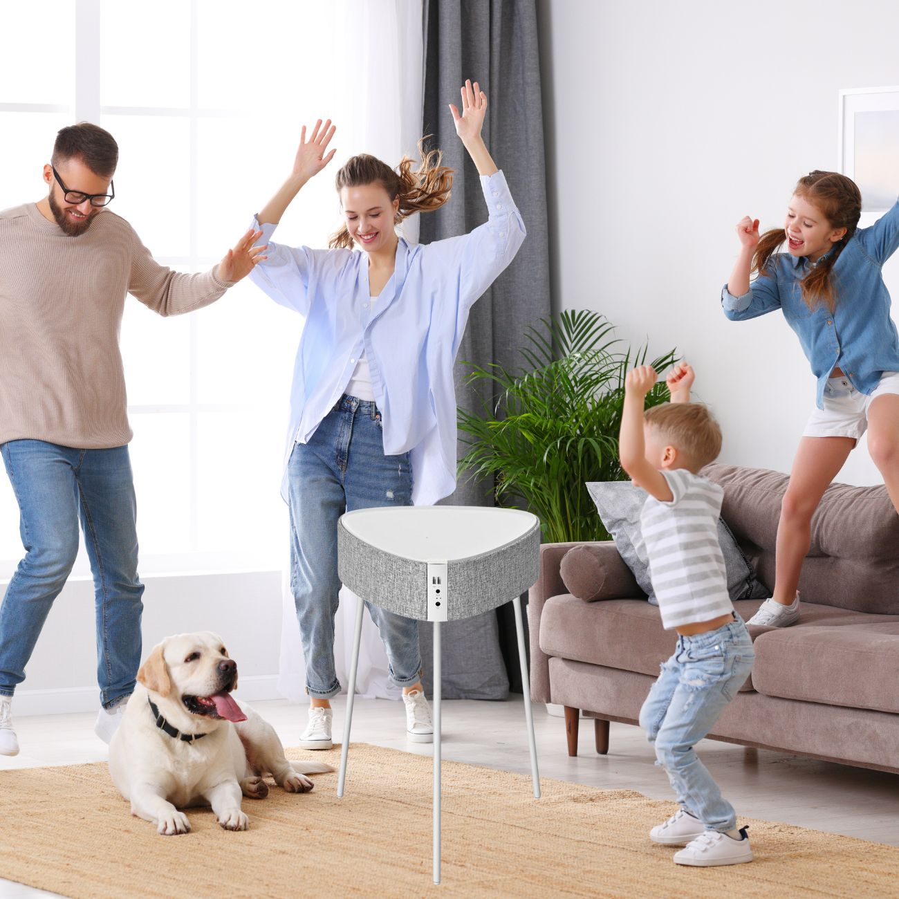 Familie tanzt um einen Lautsprecher. Hund liegt. Szene in hellem Wohnzimmer.