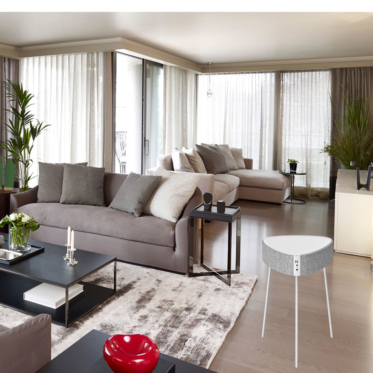 Wohnzimmer mit Sofa, Beistelltisch, Teppichen und einem Lautsprecher. Große Fenster und Vorhänge.