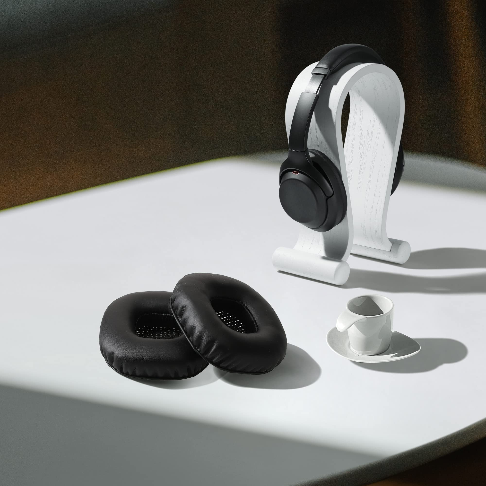 Czarne słuchawki na białym stojaku, z dwoma nausznikami i filiżanką kawy.