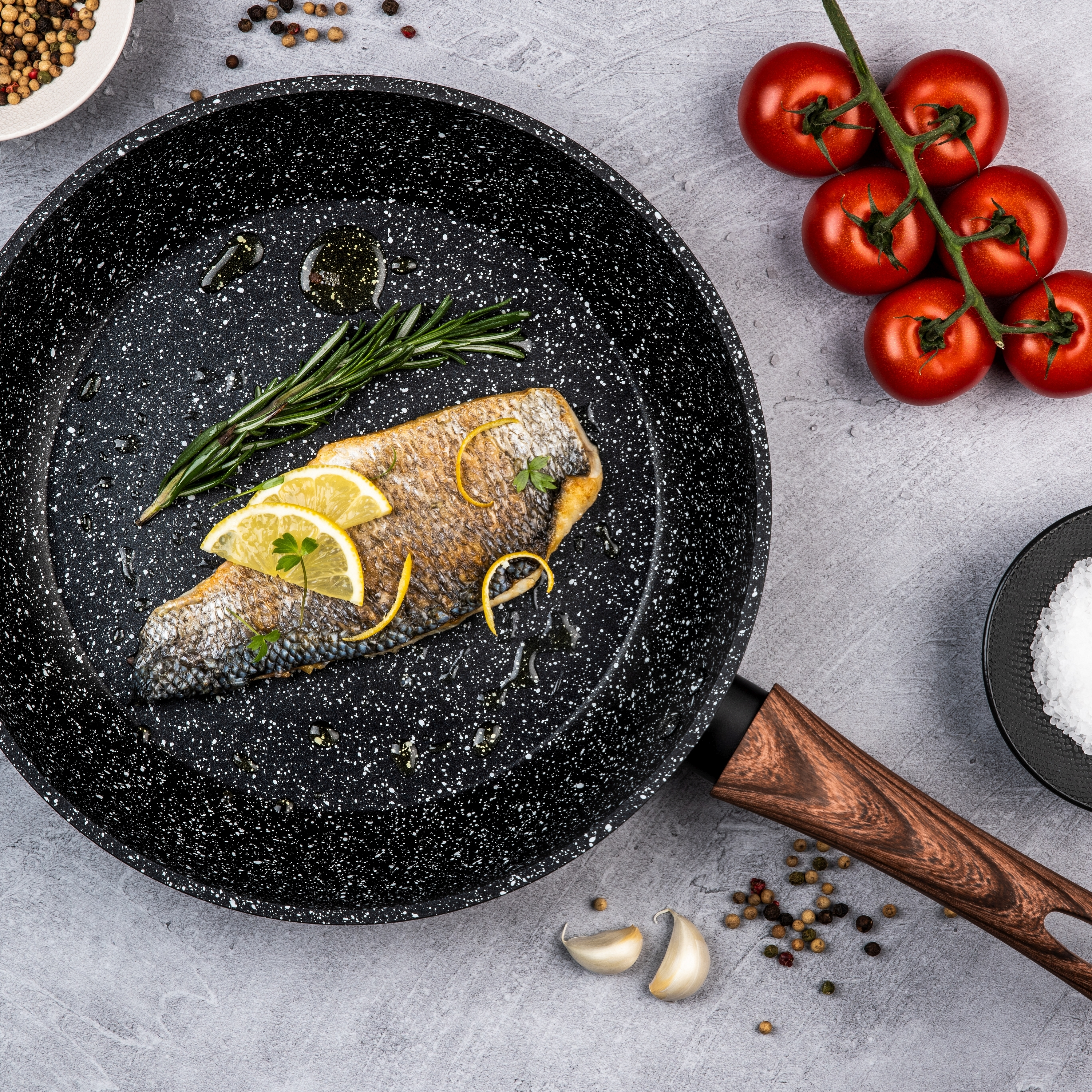 Pfanne mit gebratenem Fisch, Zitronenscheiben, Rosmarin, Tomaten und Gewürzen. Draufsicht.