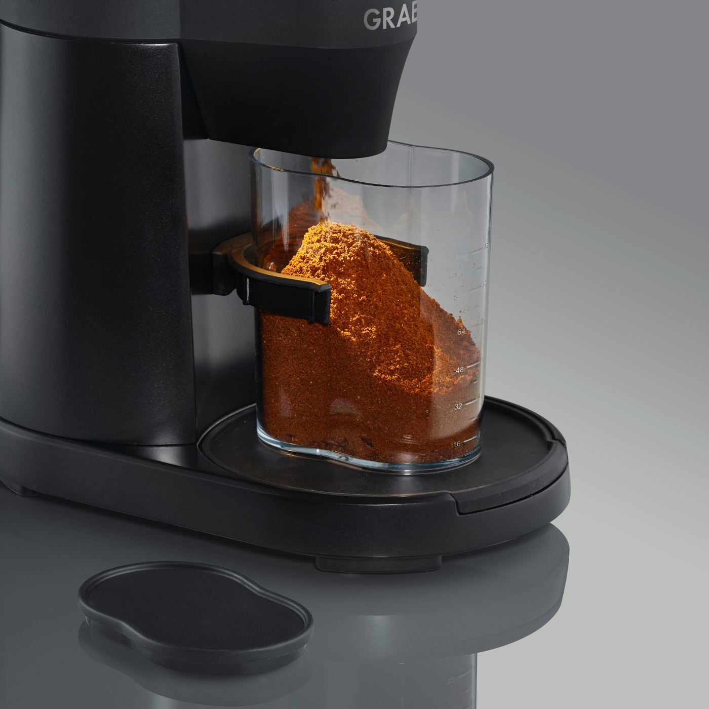 Primo piano di una macchina da caffè che eroga caffè macinato in un contenitore trasparente su una base nera.