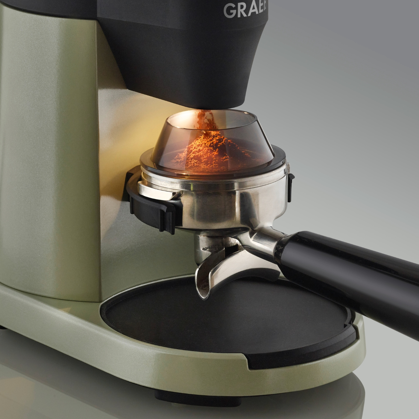 Macinacaffè con caffè macinato visibile. Base verde chiaro con parte superiore nera e manico.