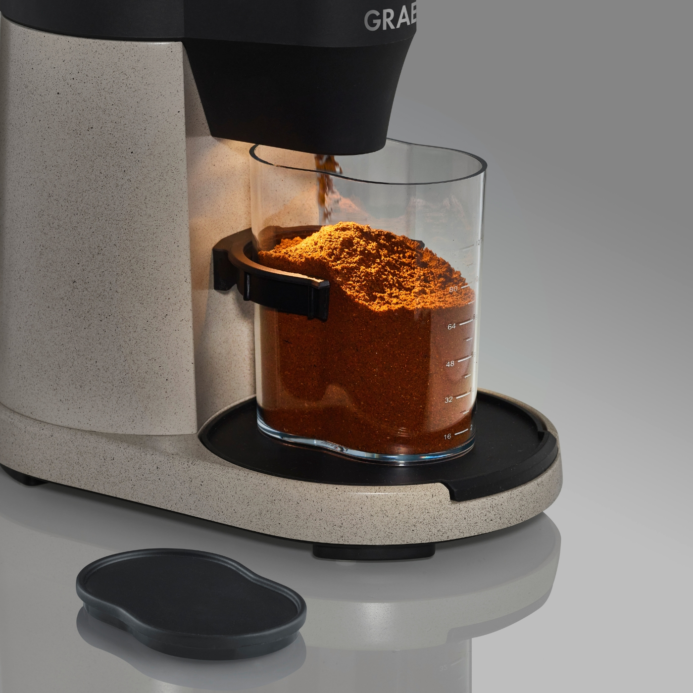 Nahaufnahme einer Kaffeemühle, die gemahlenen Kaffee in einen Glasbehälter abgibt.