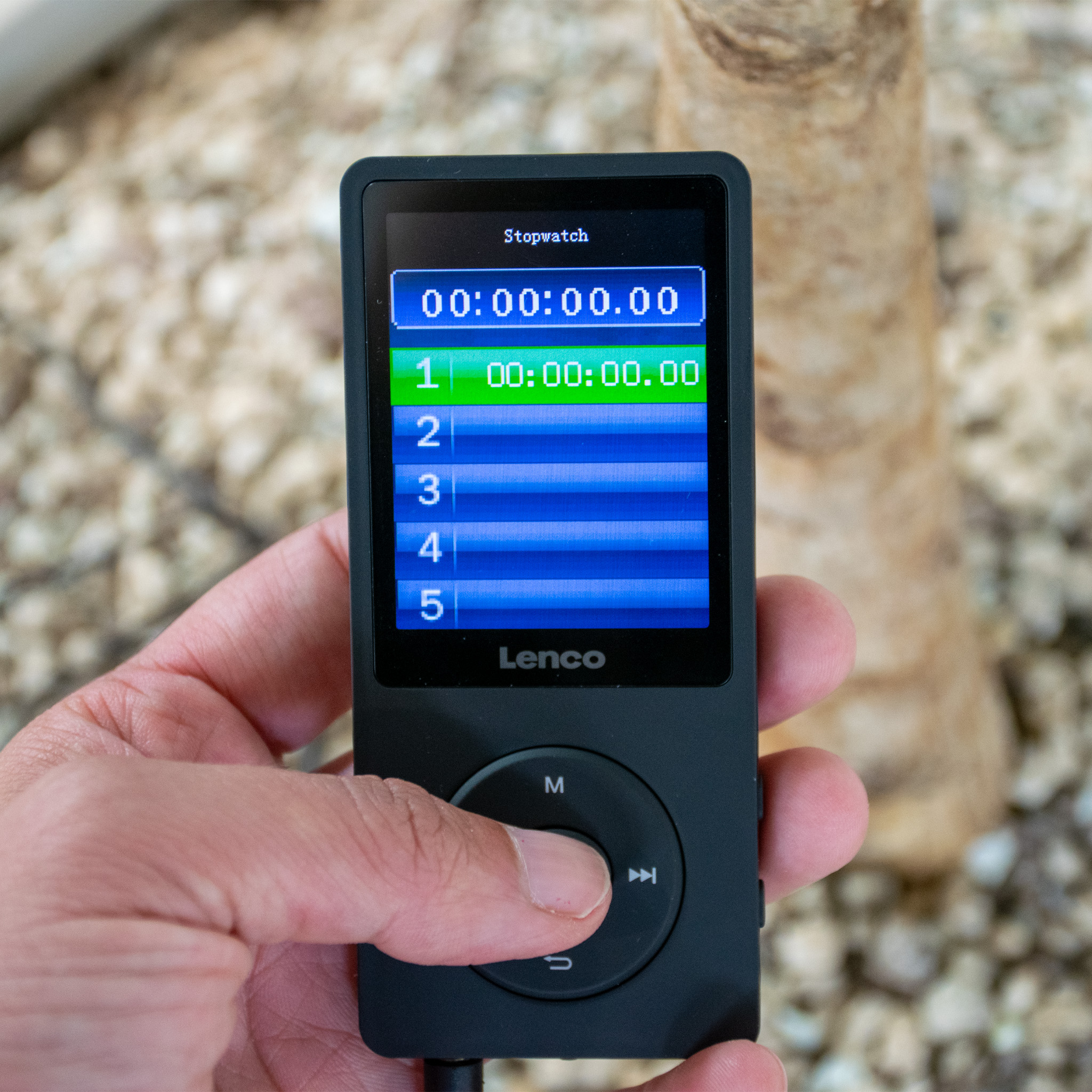 Black stopwatch device with green screen displaying timer. Held in hand.