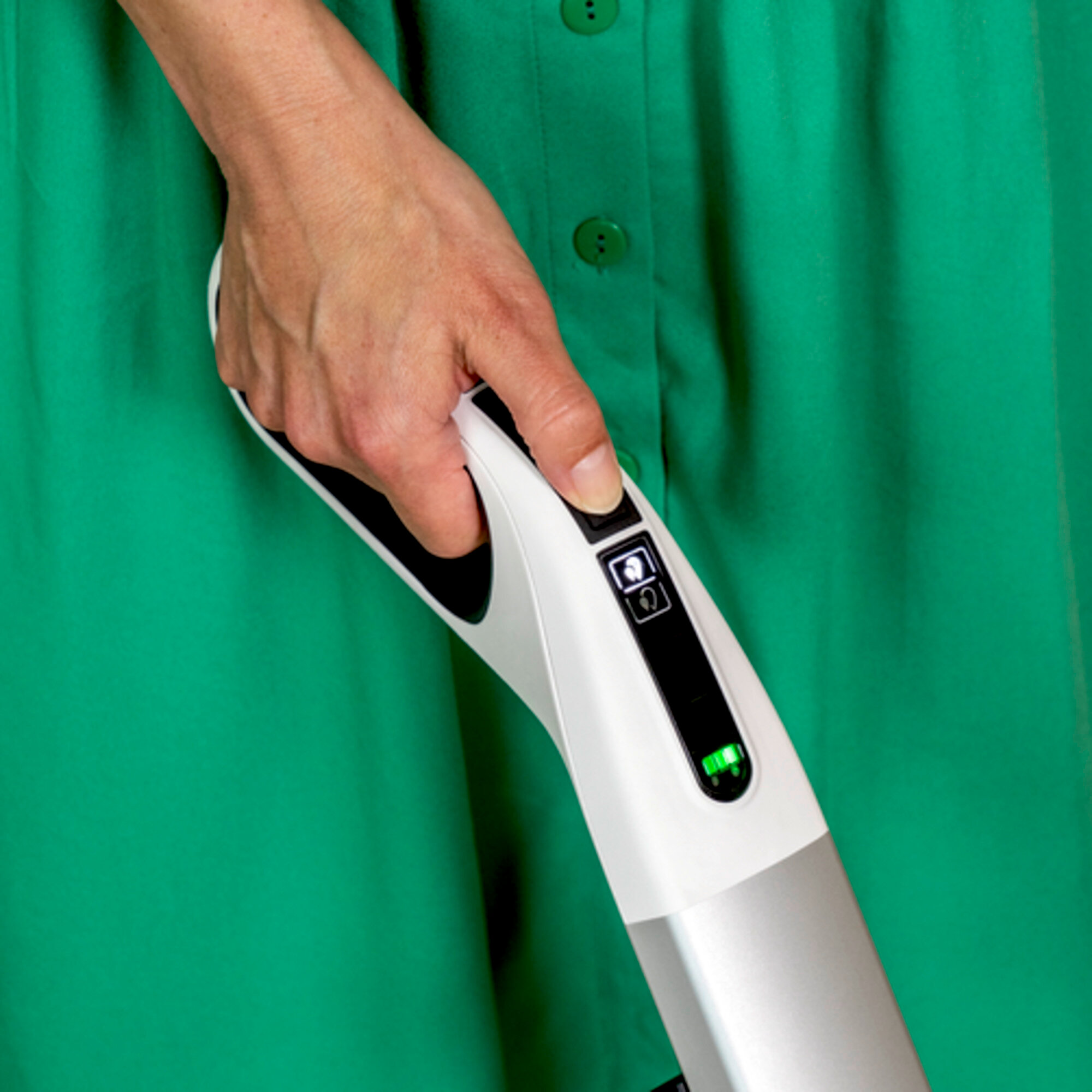Mano di una persona che tiene un aspirapolvere. Donna con un vestito verde. Il pulsante di accensione è premuto.