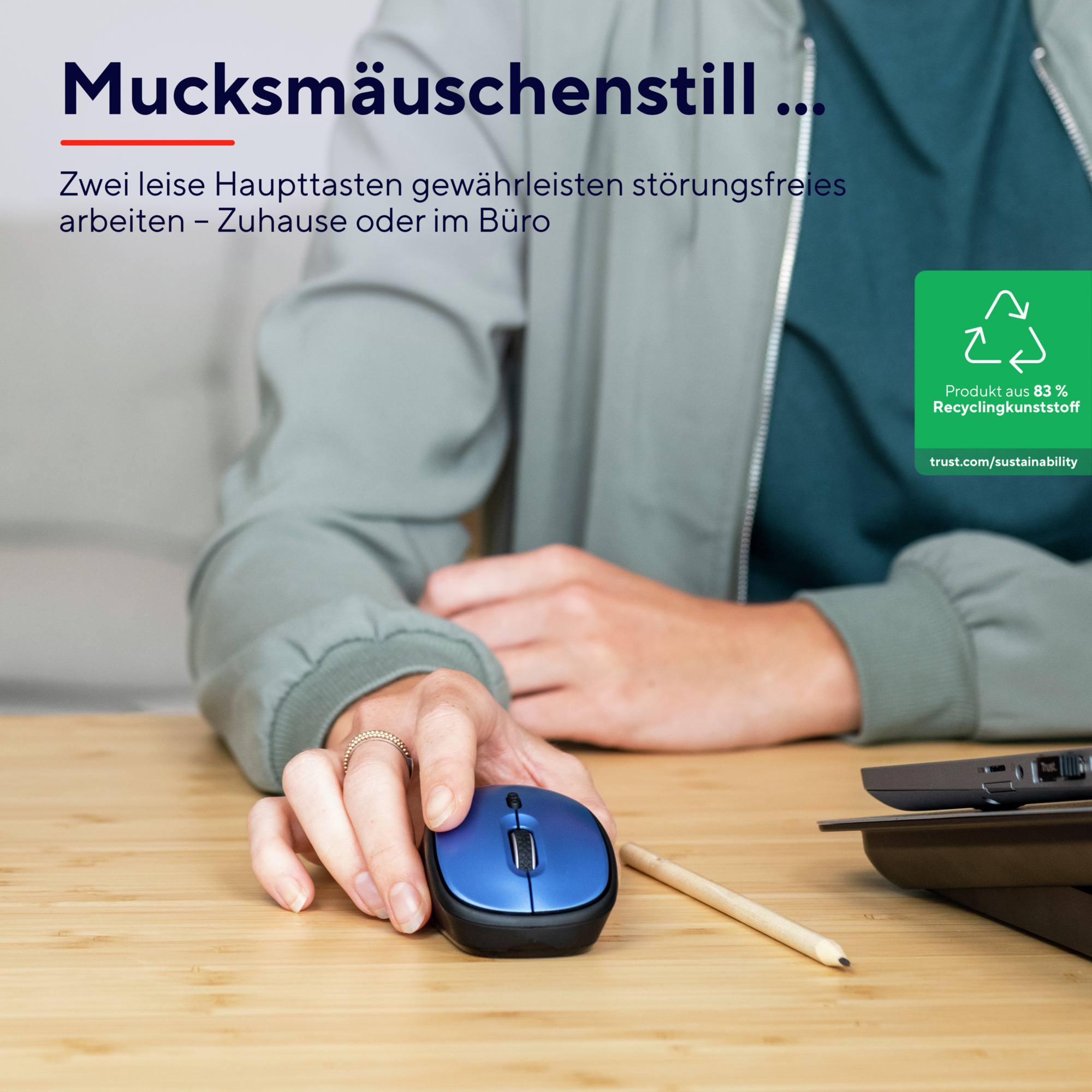 Osoba trzymająca niebieską mysz na drewnianym biurku. Widoczny jest również laptop.