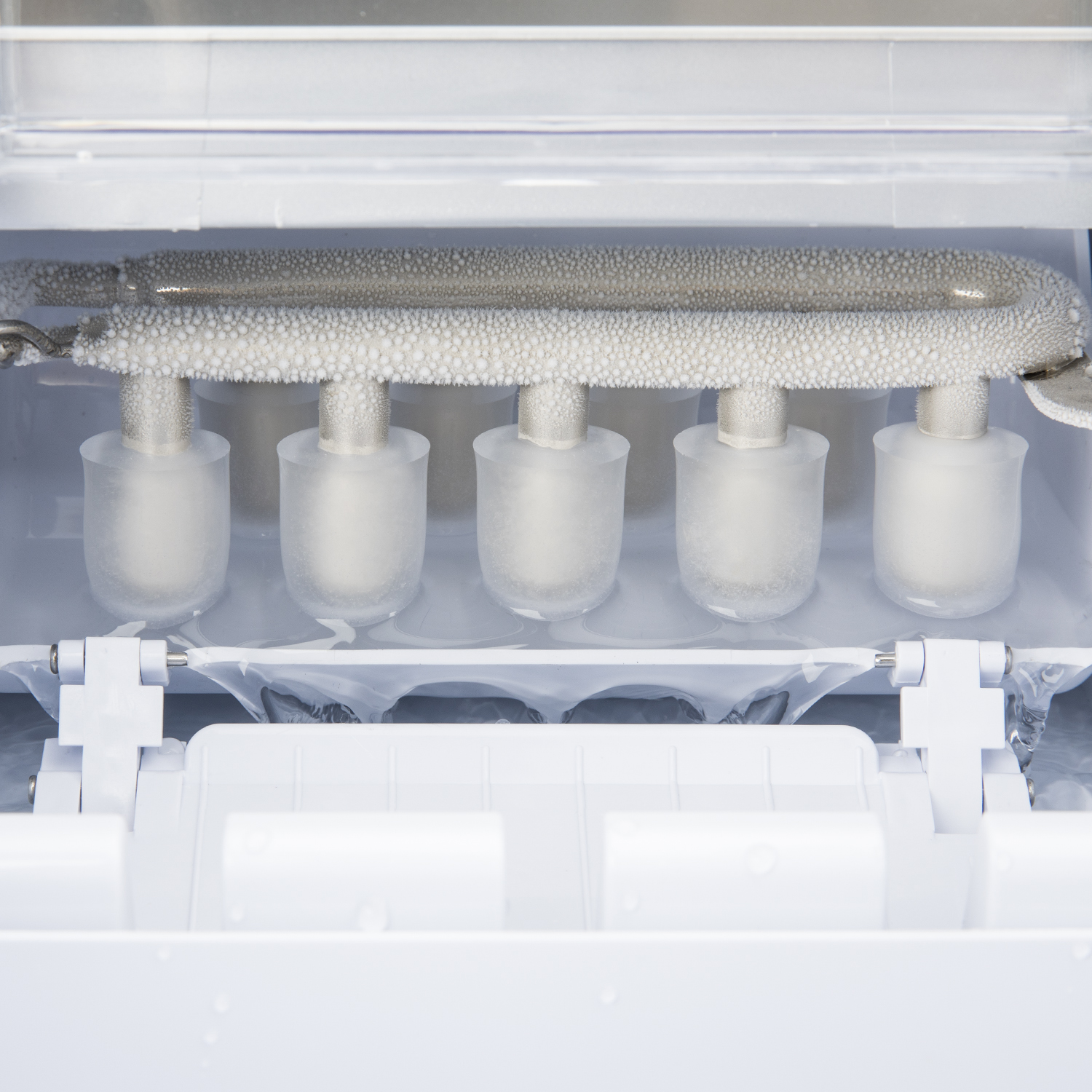 Primo piano di una macchina per il ghiaccio. Il ghiaccio si forma attorno a barre di metallo. All'interno di un elettrodomestico bianco.