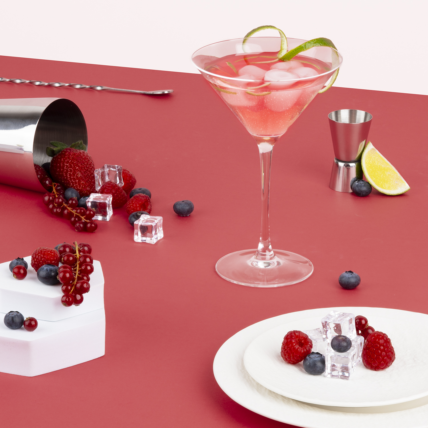 Cocktail con frutta e cubetti di ghiaccio su superficie rossa. Shaker, jigger e piatto con bacche.