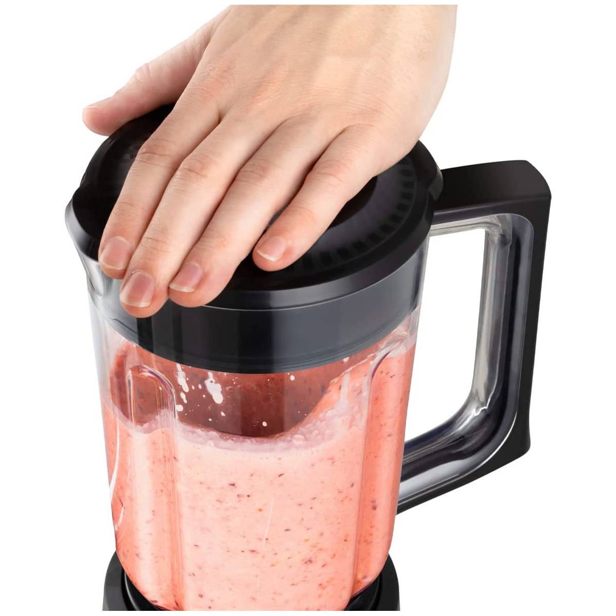 Mano sul coperchio nero del frullatore. Frullatore con liquido rosa. Sfondo bianco.
