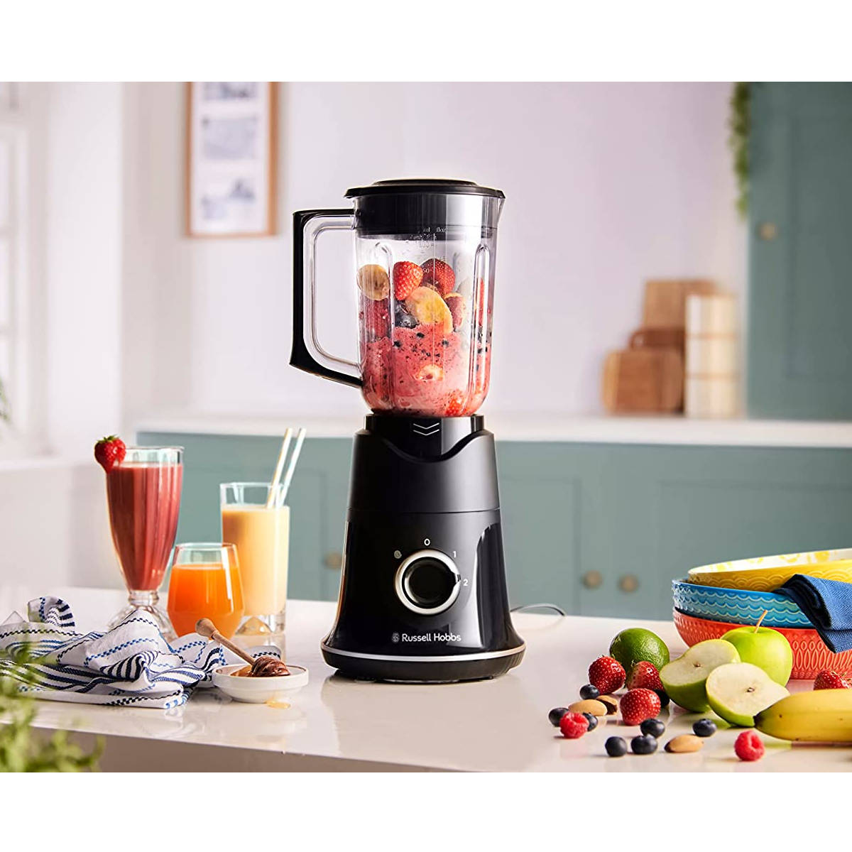 Frullatore nero con un contenitore pieno di frutta rossa e un frullato. La frutta è disposta intorno.