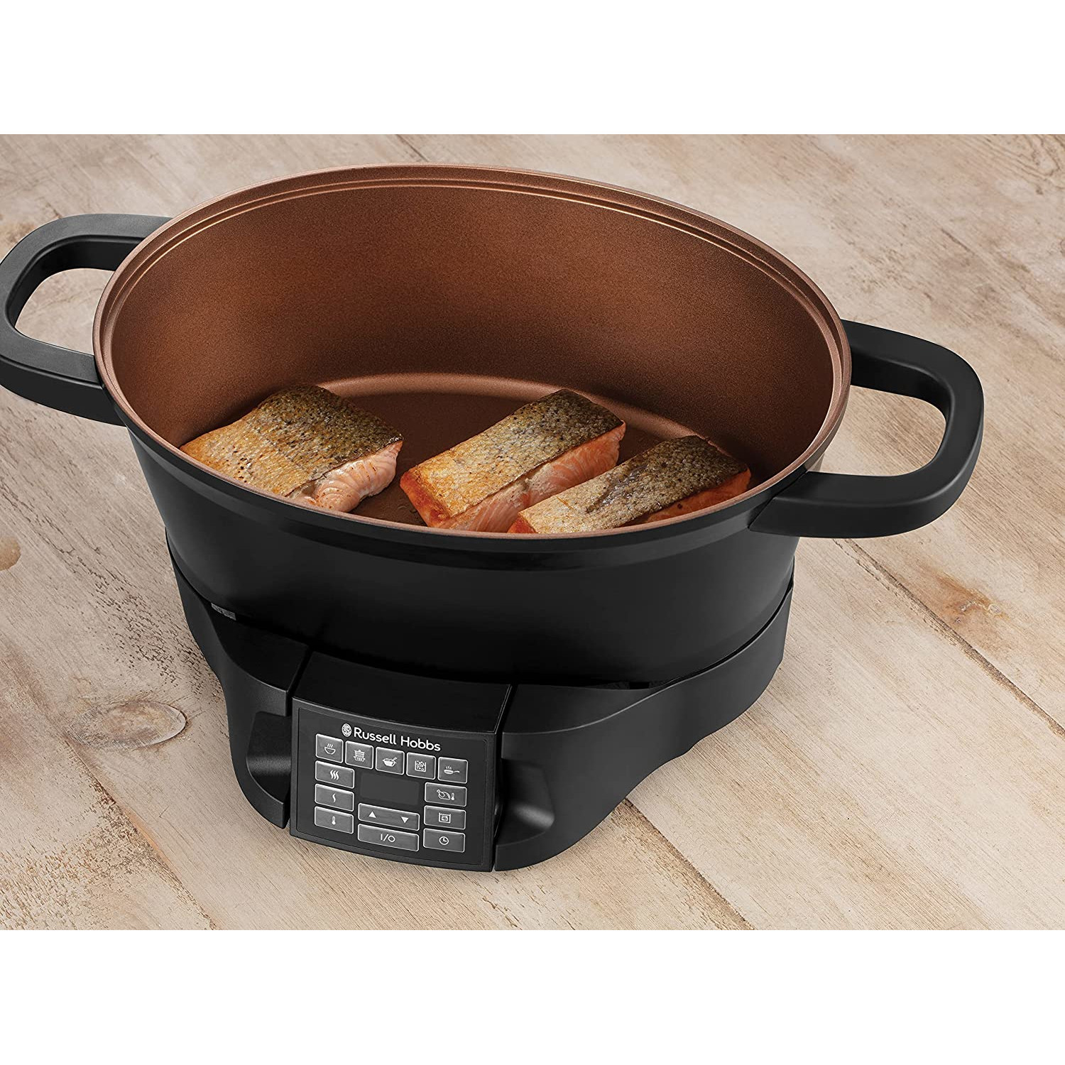 Siyah ve bakır renkli Russell Hobbs yavaş pişirici. İçinde üç parça pişmiş somon balığı var. Ahşap bir yüzeyin üzerinde duruyor.