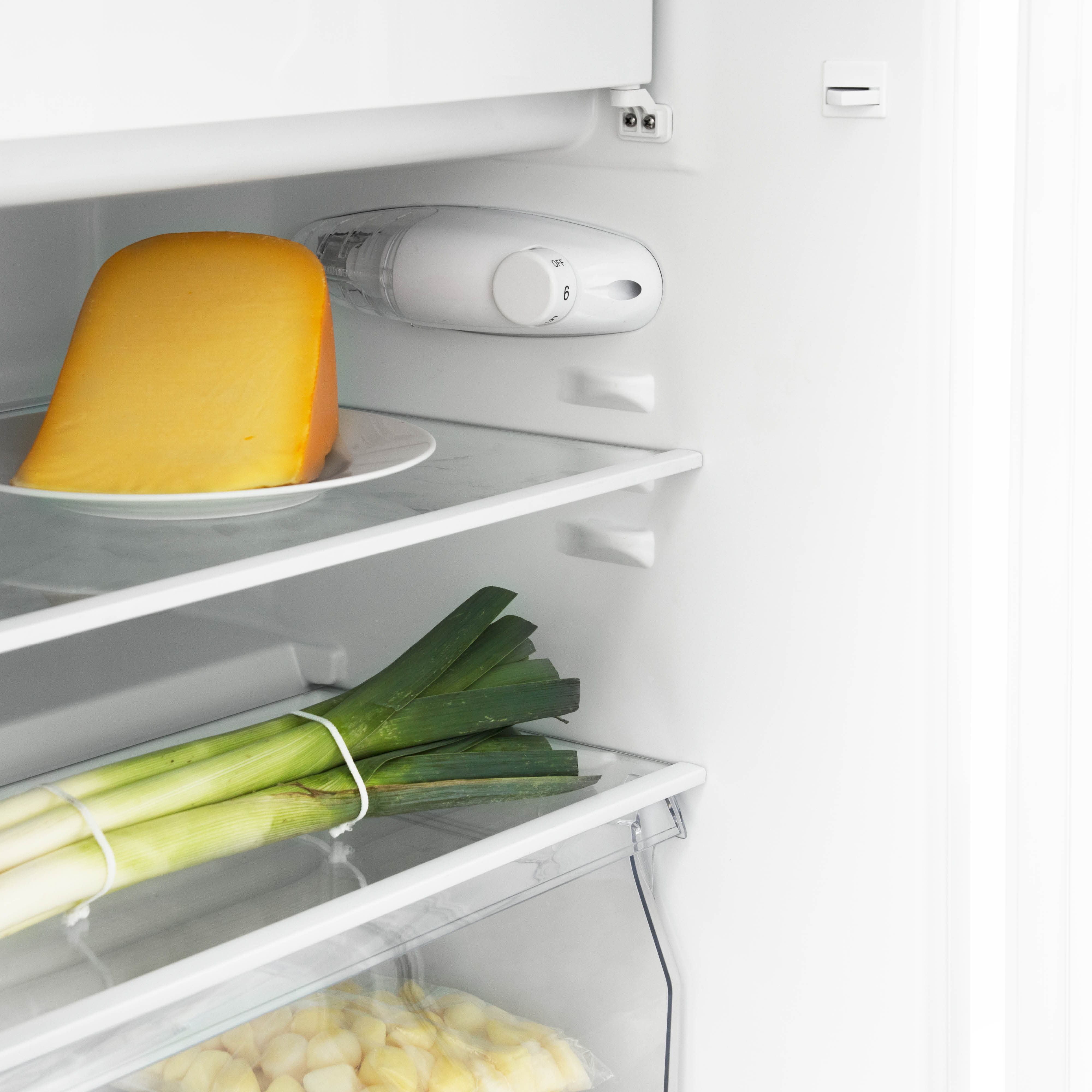 Koelkastinterieur: kaas op bord, prei gebonden, en plastic zak met aardappelen.