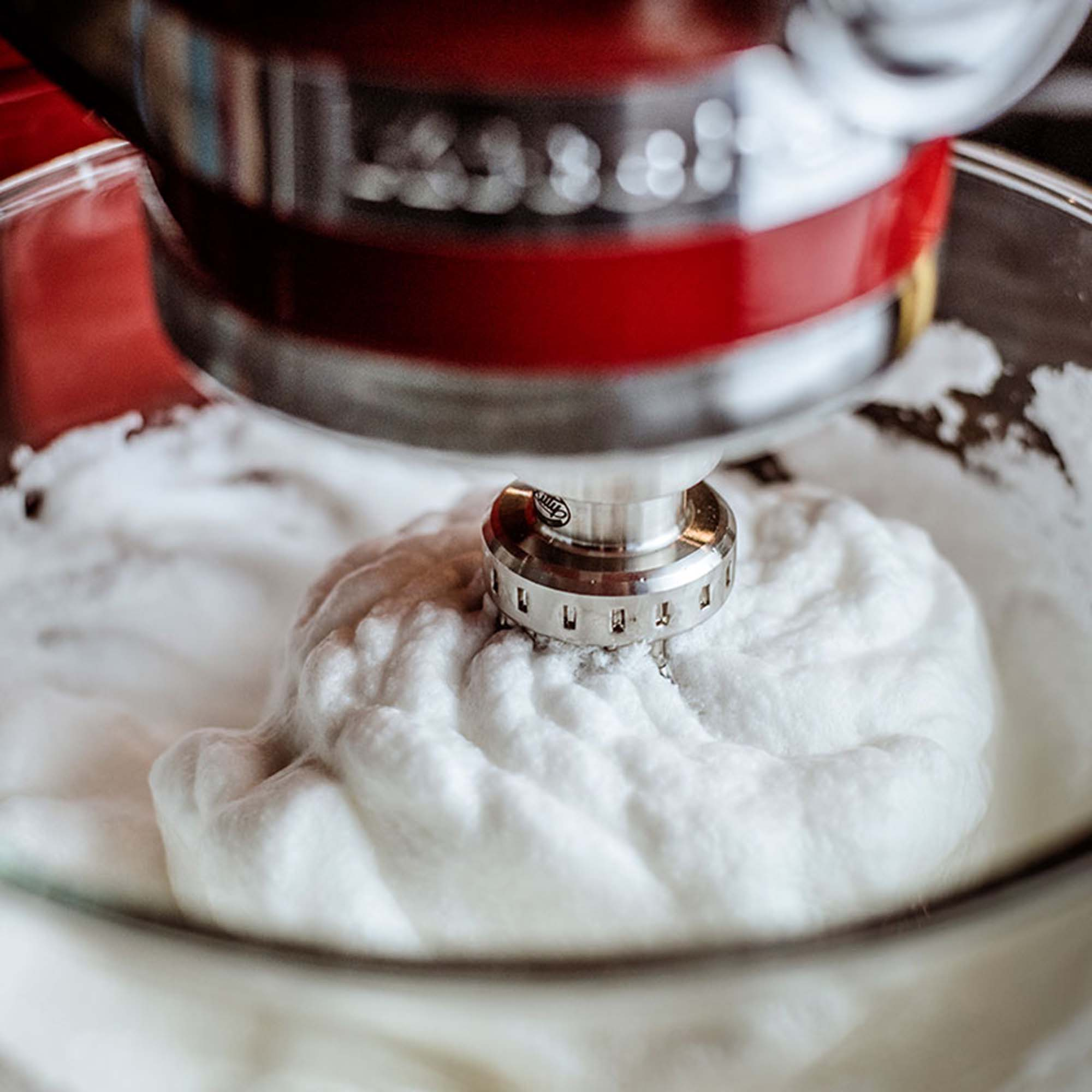 Ein roter KitchenAid-Mixer mit Schneebesenaufsatz in einer Glasschüssel mit Schlagsahne.