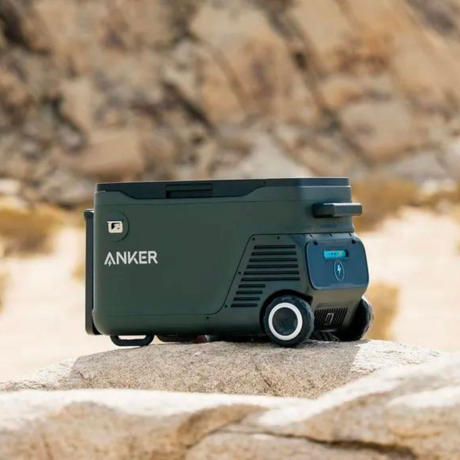 Przenośna lodówko-zamrażarka Anker na skalistym krajobrazie. Lodówka jest oliwkowozielona z kołami i uchwytem.