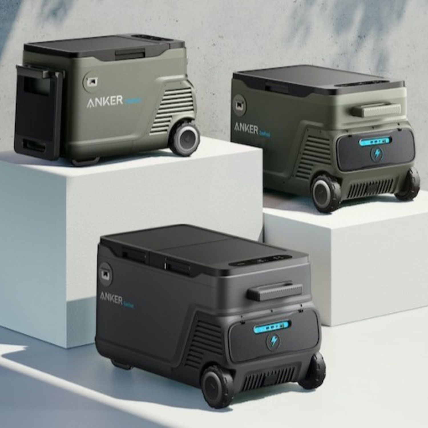 Trzy przenośne stacje zasilania Anker. Zielone i czarne, z kołami i panelami słonecznymi na górze.