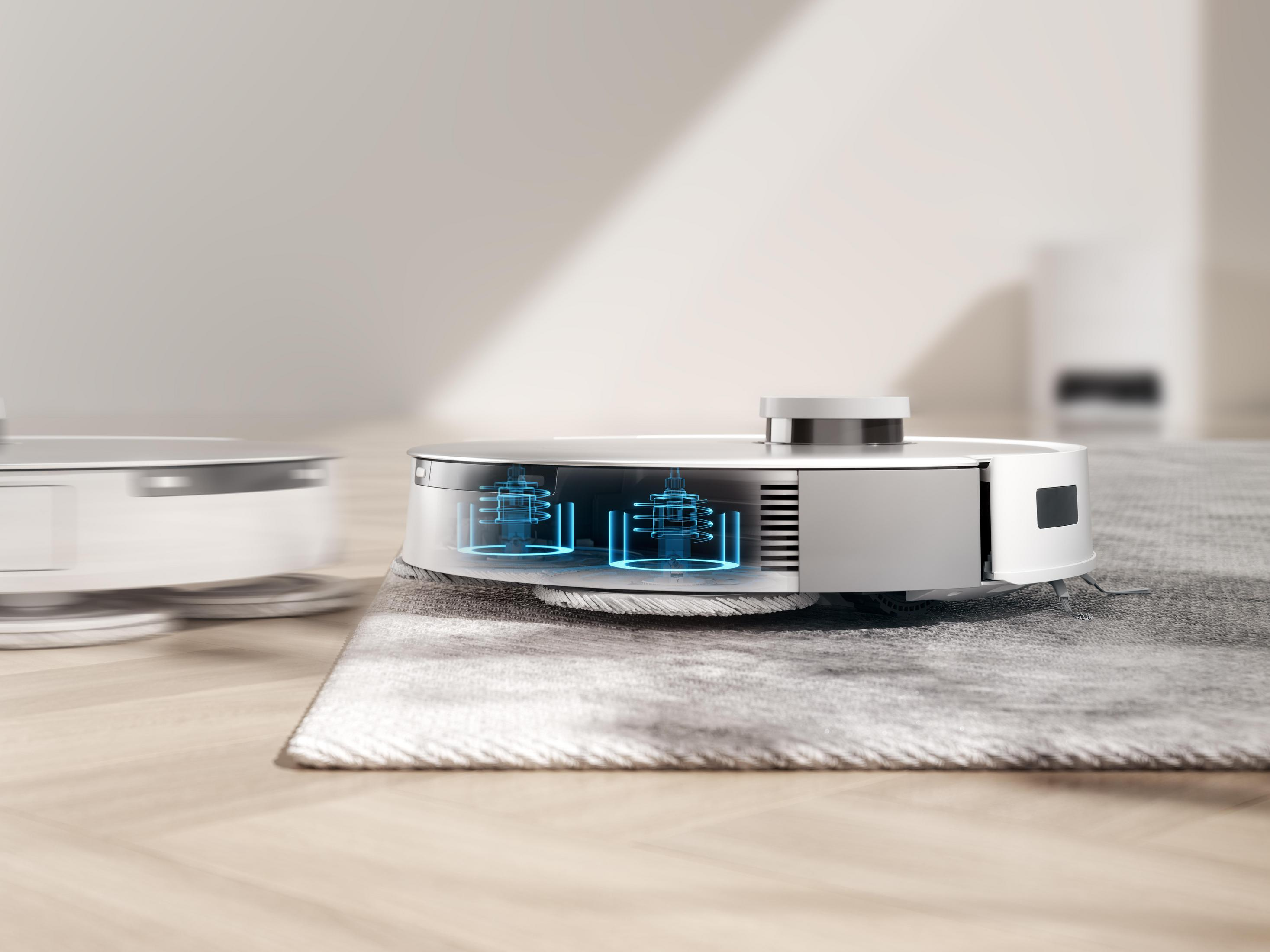 Srebrny odkurzacz robot sprząta szary dywan na drewnianej podłodze.