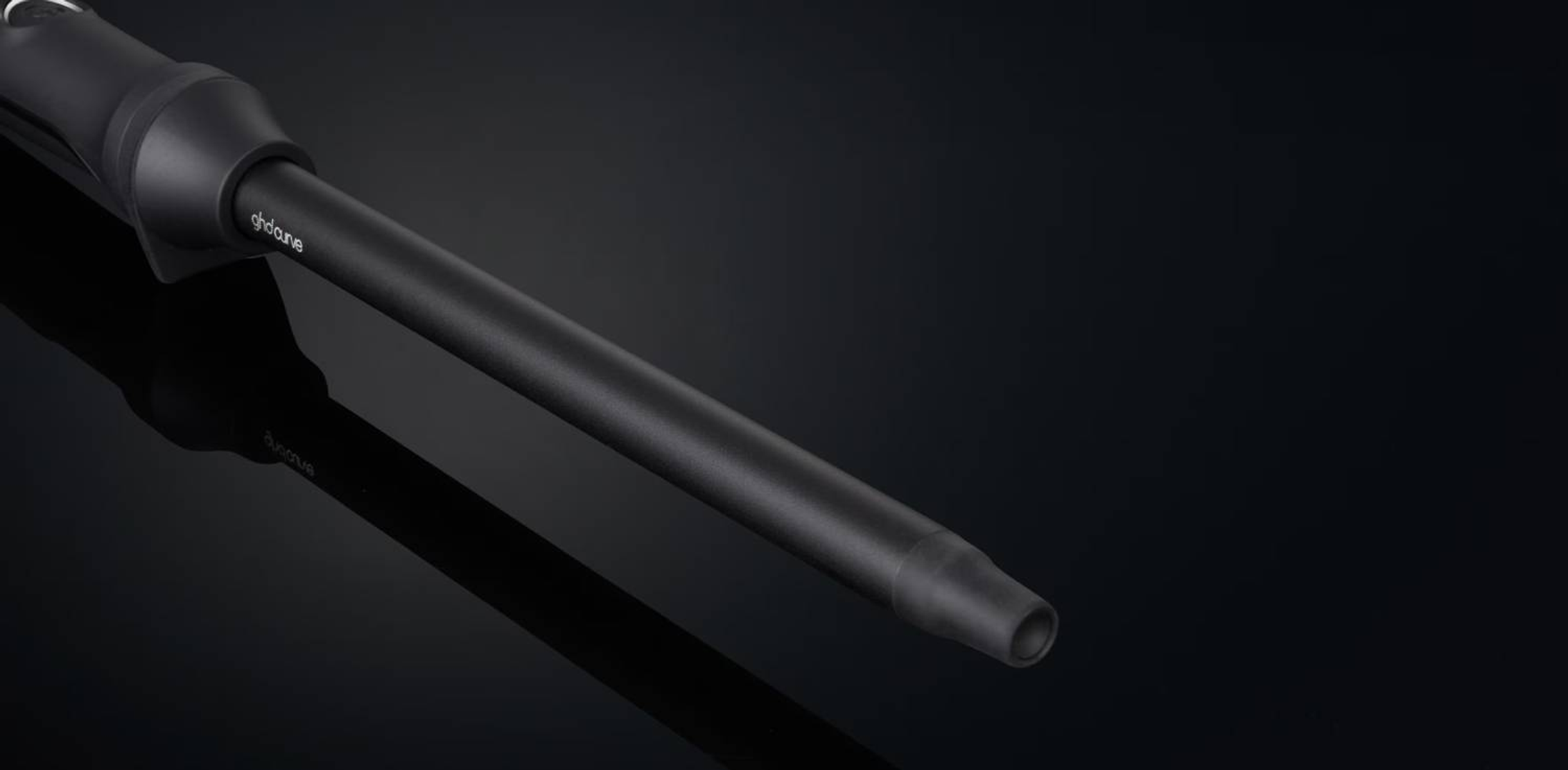 Un rizador negro con la marca 'ghdcurve' visible, sobre una superficie negra.