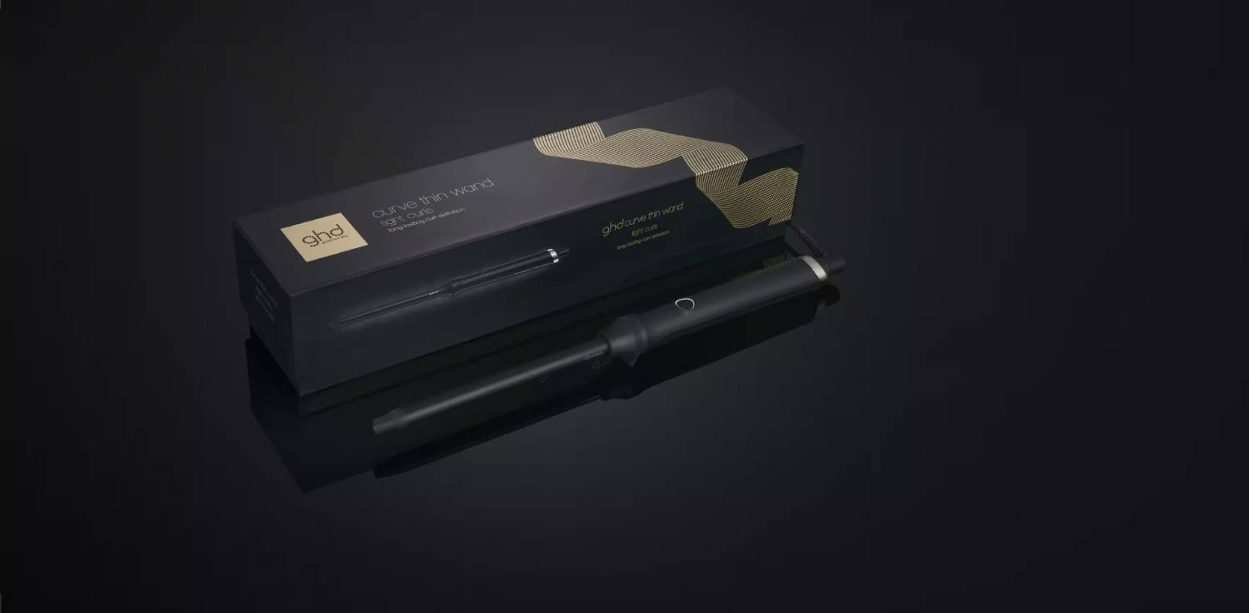 Rizador negro y caja sobre una superficie negra. La marca GHD es visible.