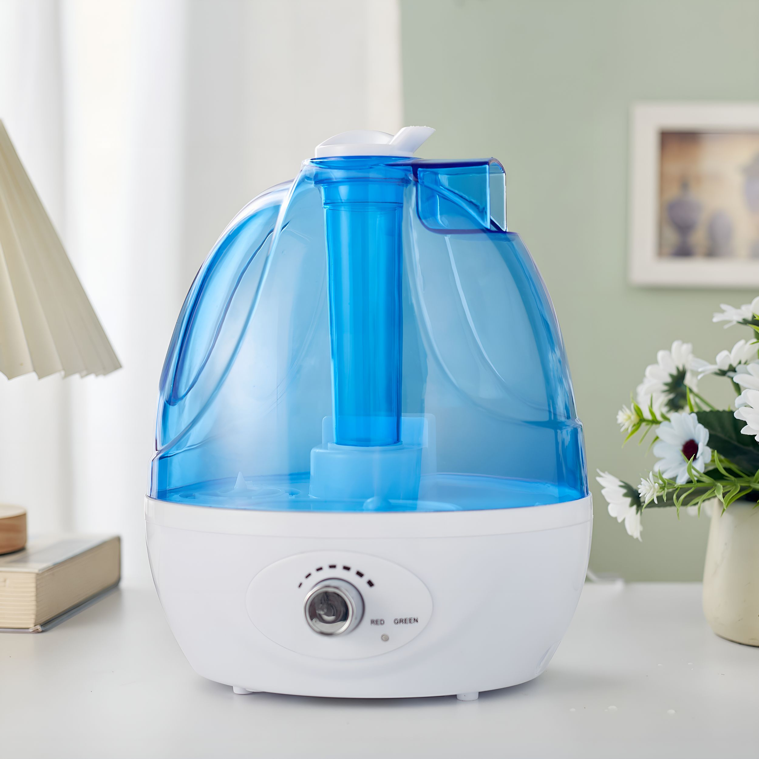 Ein weiß-blauer Luftbefeuchter mit Wassertank, Bedienknopf und Blumen im Hintergrund.