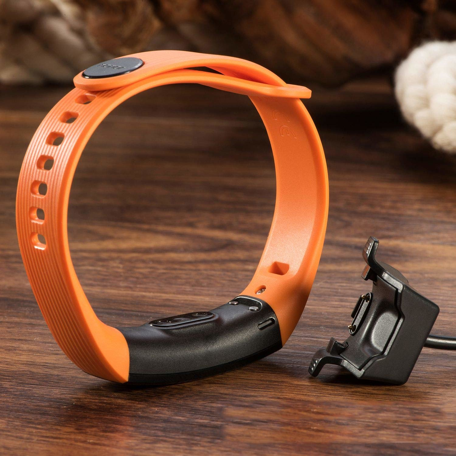 Ein orangefarbenes Smartwatch-Armband mit einem schwarzen Modul und Ladegerät. Das Band ist gebogen.