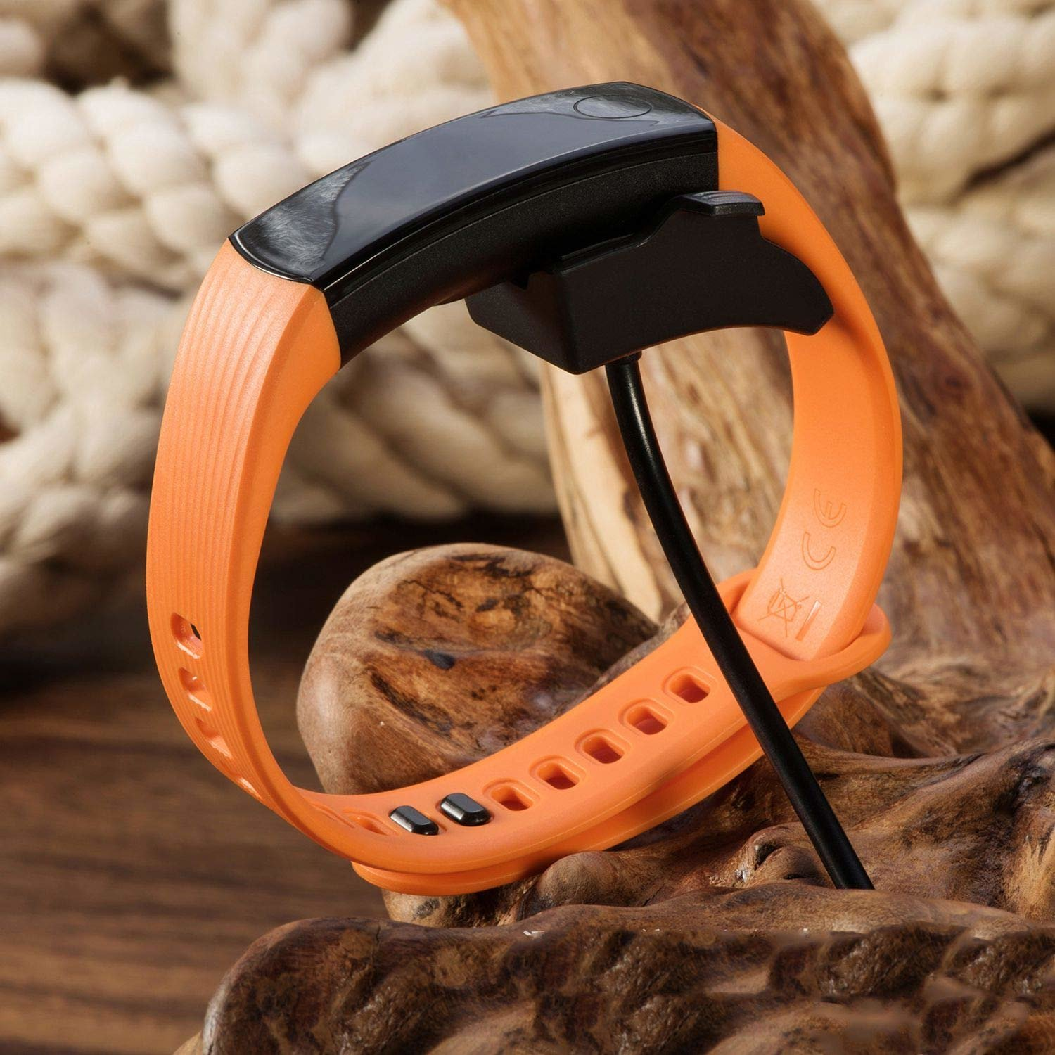 Oranger Fitness-Tracker mit schwarzem Ladekabel und Dock auf Holzoberfläche.