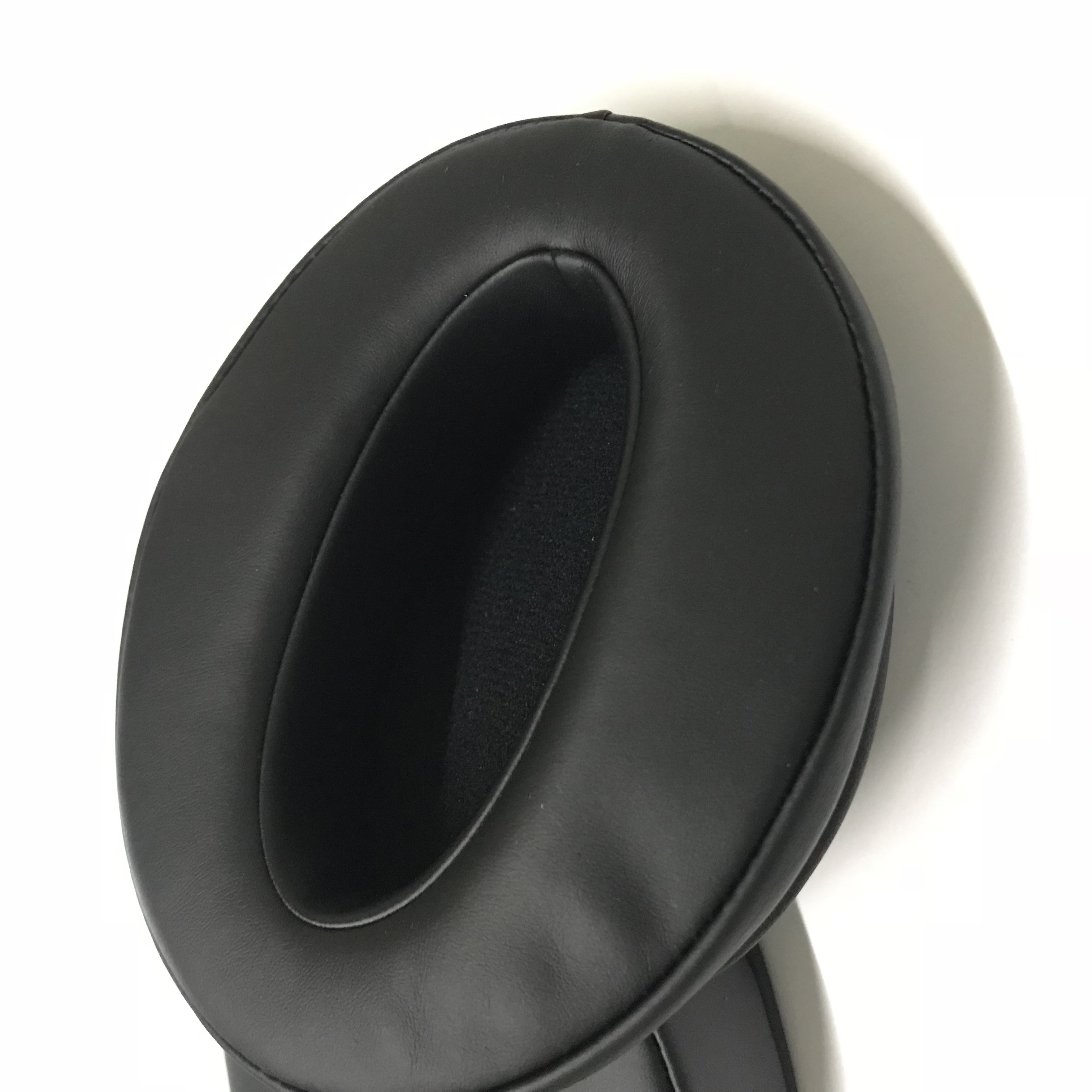 Zbliżenie czarnej poduszki nausznej słuchawek na białej powierzchni. Miękkie, ciemne wnętrze.