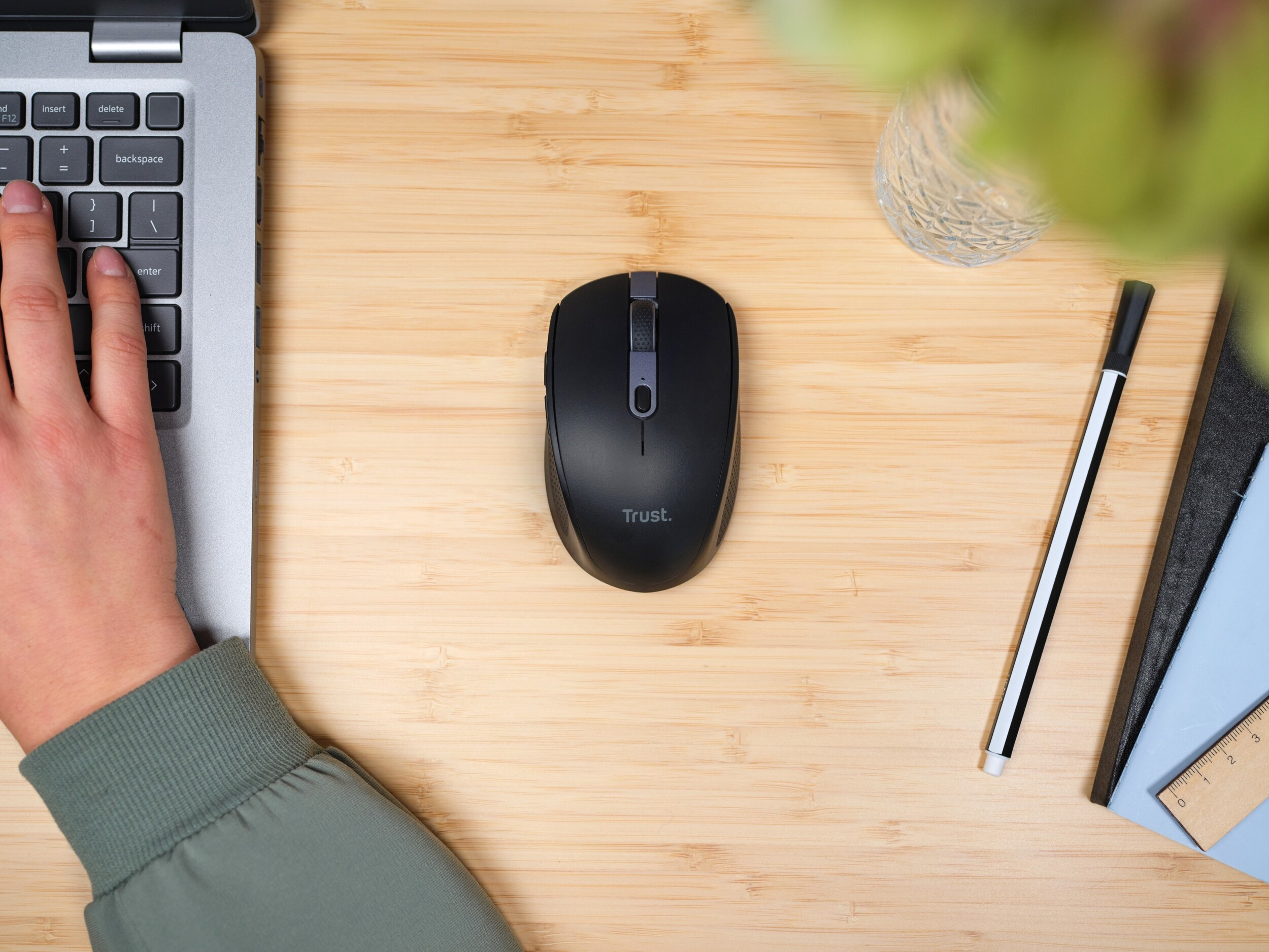 Ręka obok klawiatury laptopa i czarna mysz na drewnianym biurku.