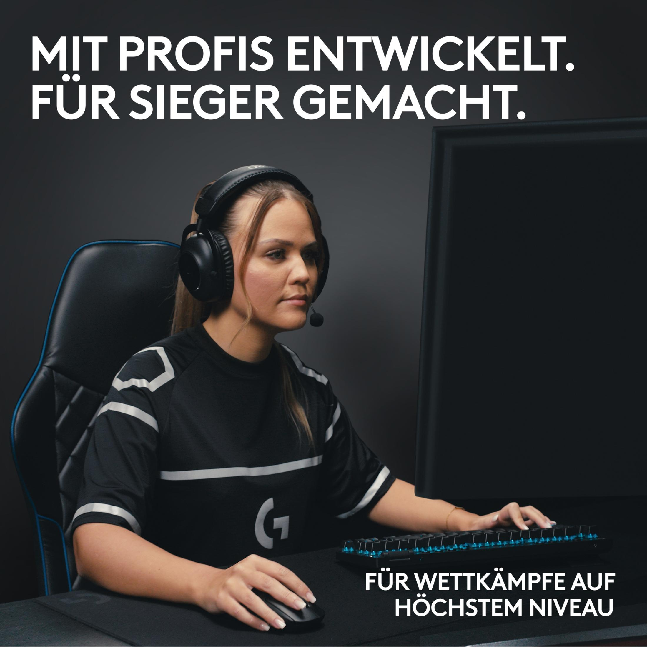 Kobieta ze słuchawkami i mikrofonem gra w grę. Siedzi przy biurku z klawiaturą.