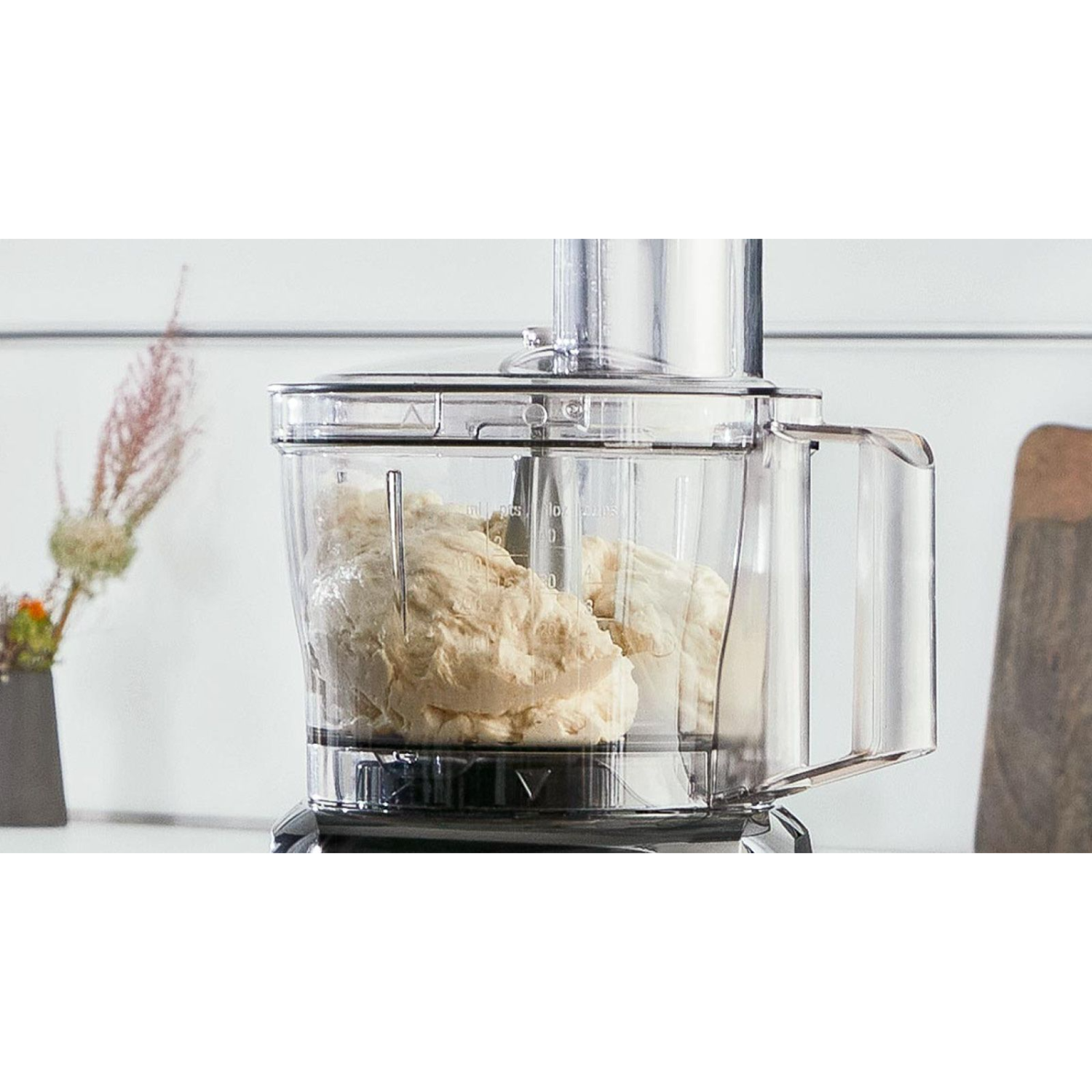 Robot kuchenny z ciastem wewnątrz przezroczystej miski. Białe tło z małą rośliną.