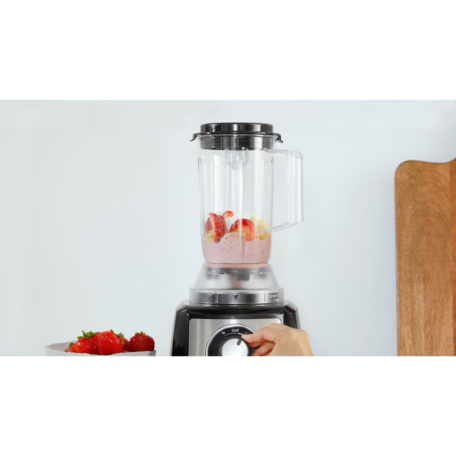 Blender z truskawkami i innymi owocami w trakcie miksowania. Ręka obraca pokrętło zasilania blendera.