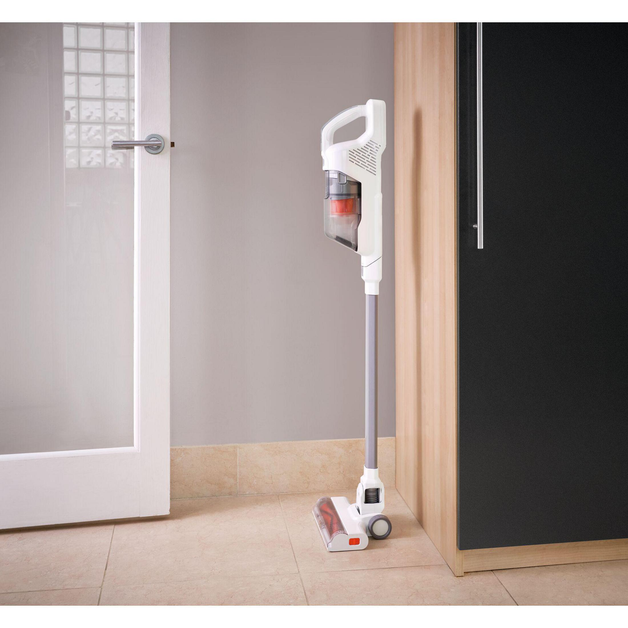 Un aspirapolvere bianco e grigio è appoggiato a un muro accanto a una porta e a un mobile nero.