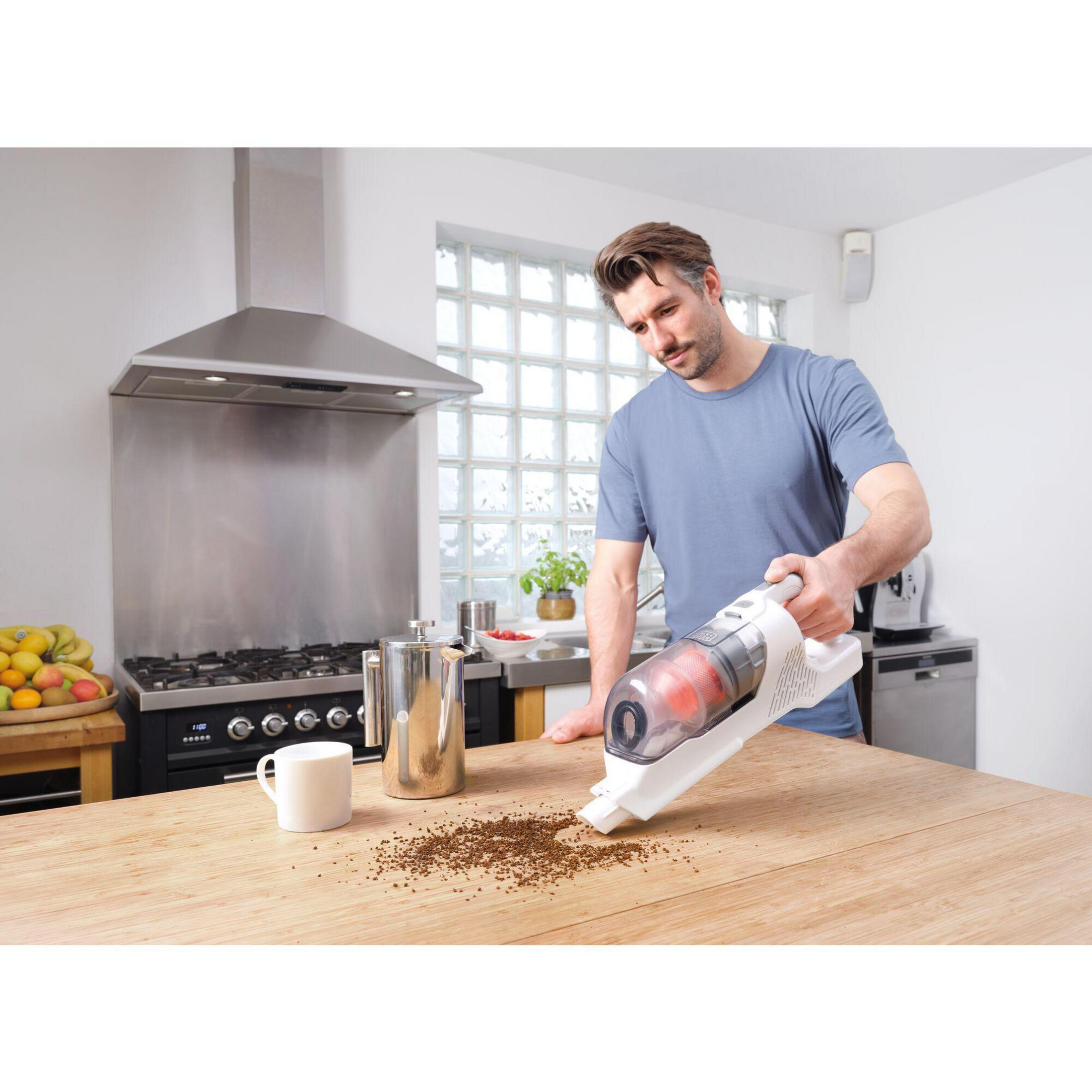 Un uomo che aspira un tavolo di legno. I fondi di caffè sono sul tavolo, con una caffettiera e una tazza.