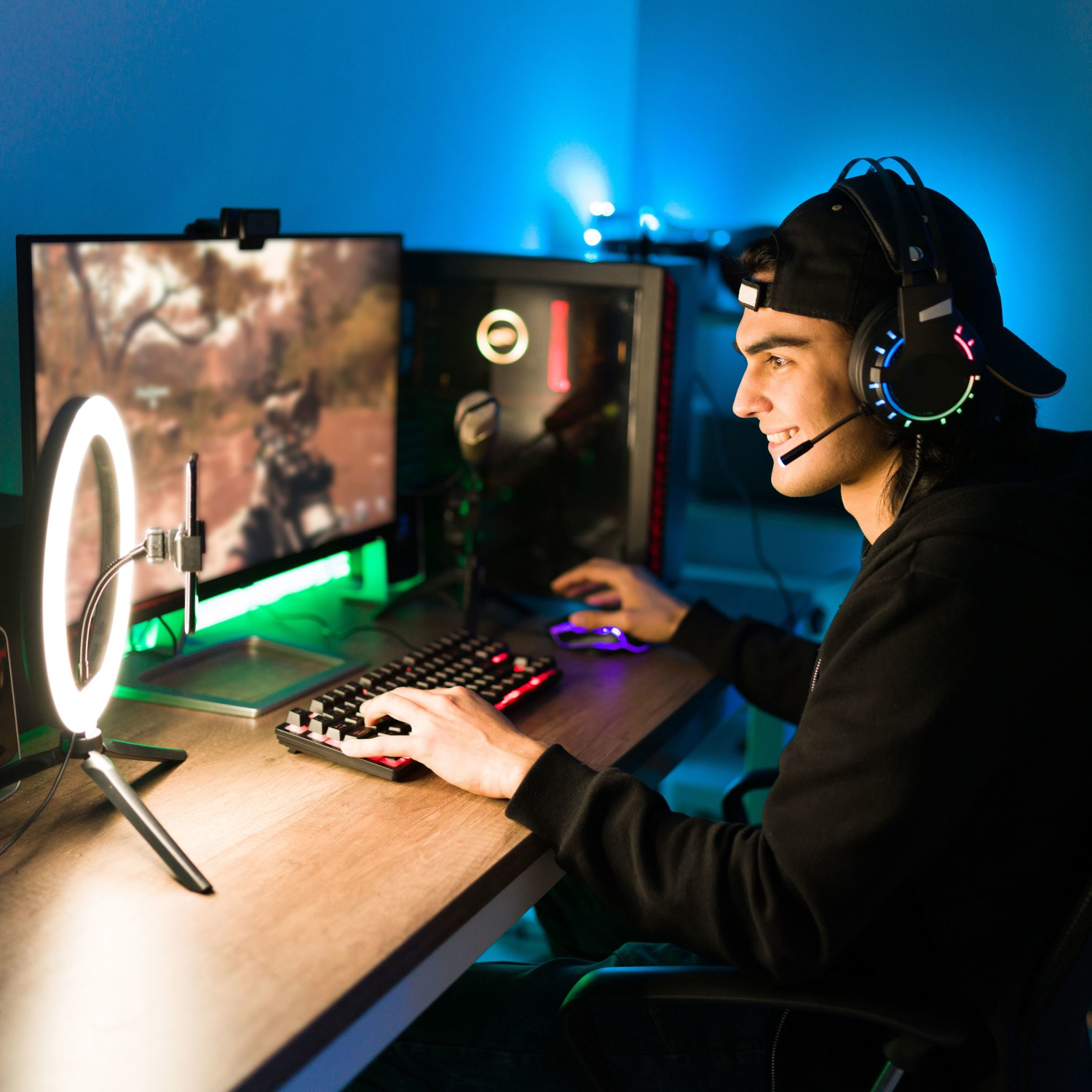 Jugador con auriculares y micrófono, jugando en un monitor. Una luz de anillo y teclado en el escritorio. Luces azules y verdes.