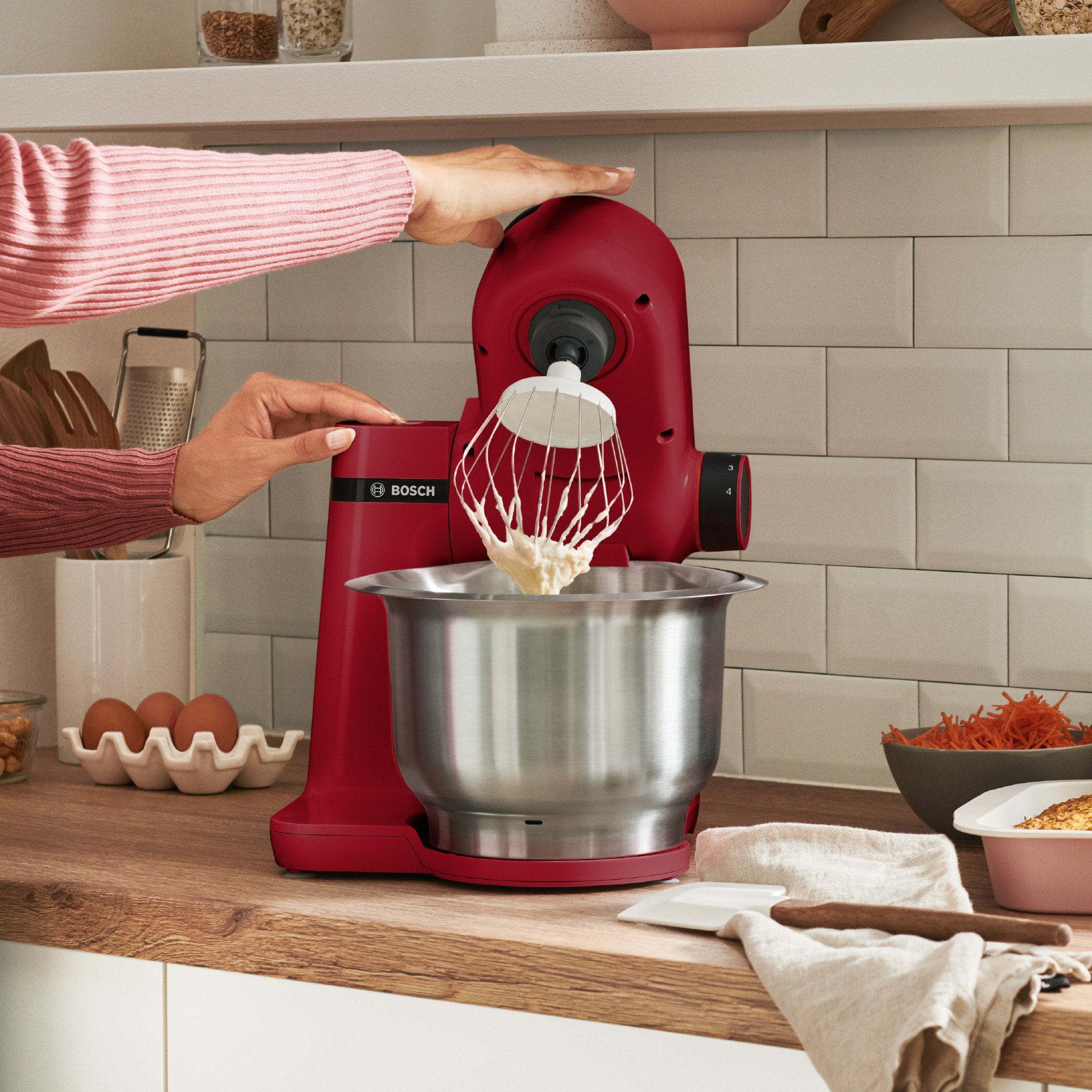 Robot pâtissier rouge avec un bol et un fouet, les mains d'une femme l'utilisent.