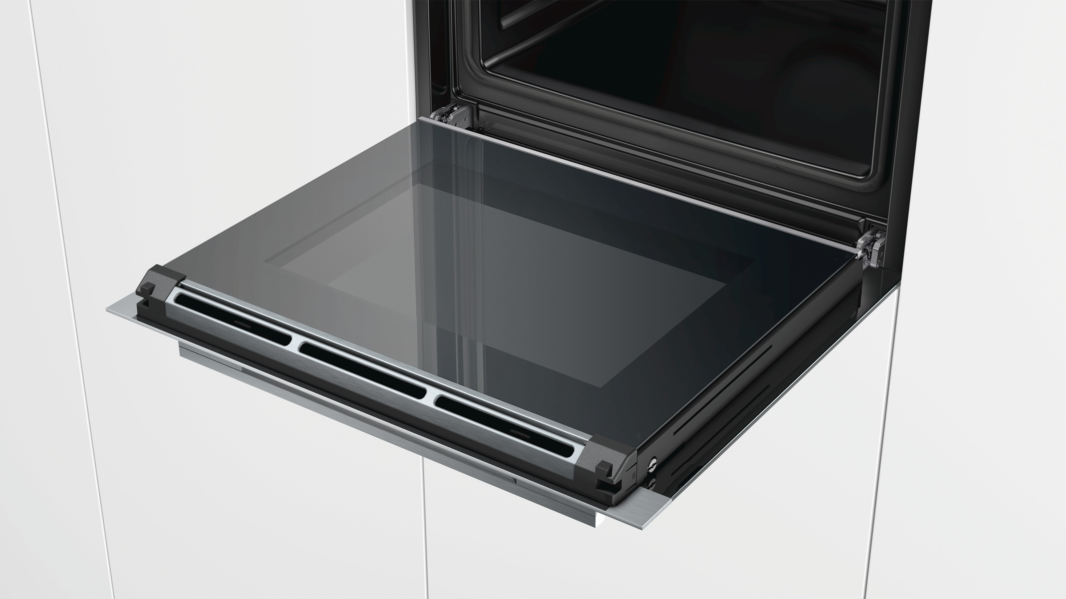 Geöffnete Glastürofen mit schwarzem Innenraum. Die Tür ist teilweise aus einem weißen Schrank herausgezogen.