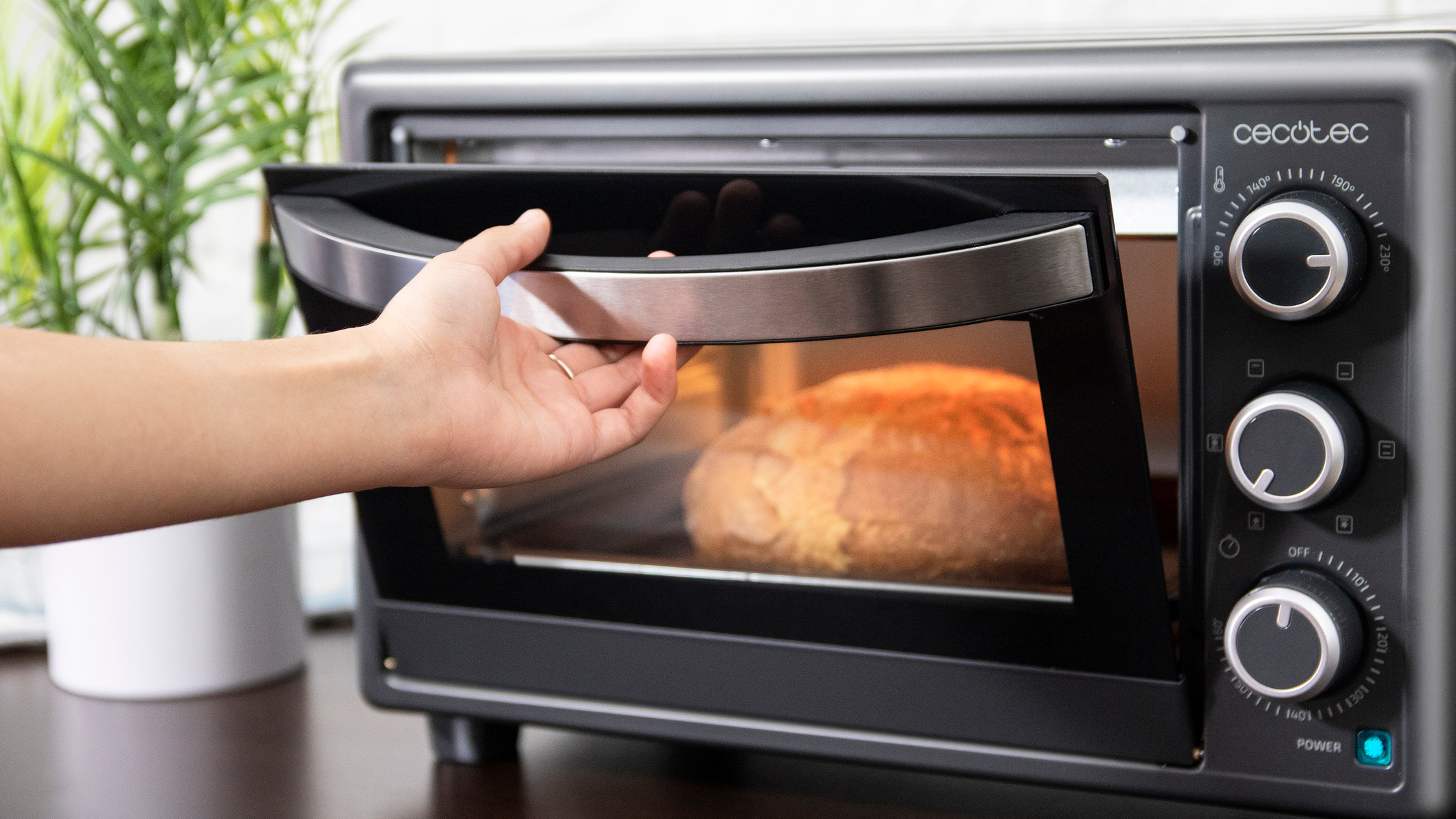 Persona che apre un forno nero. Pane dentro. Maniglia argentata, manopola di alimentazione e comandi sono sul lato.