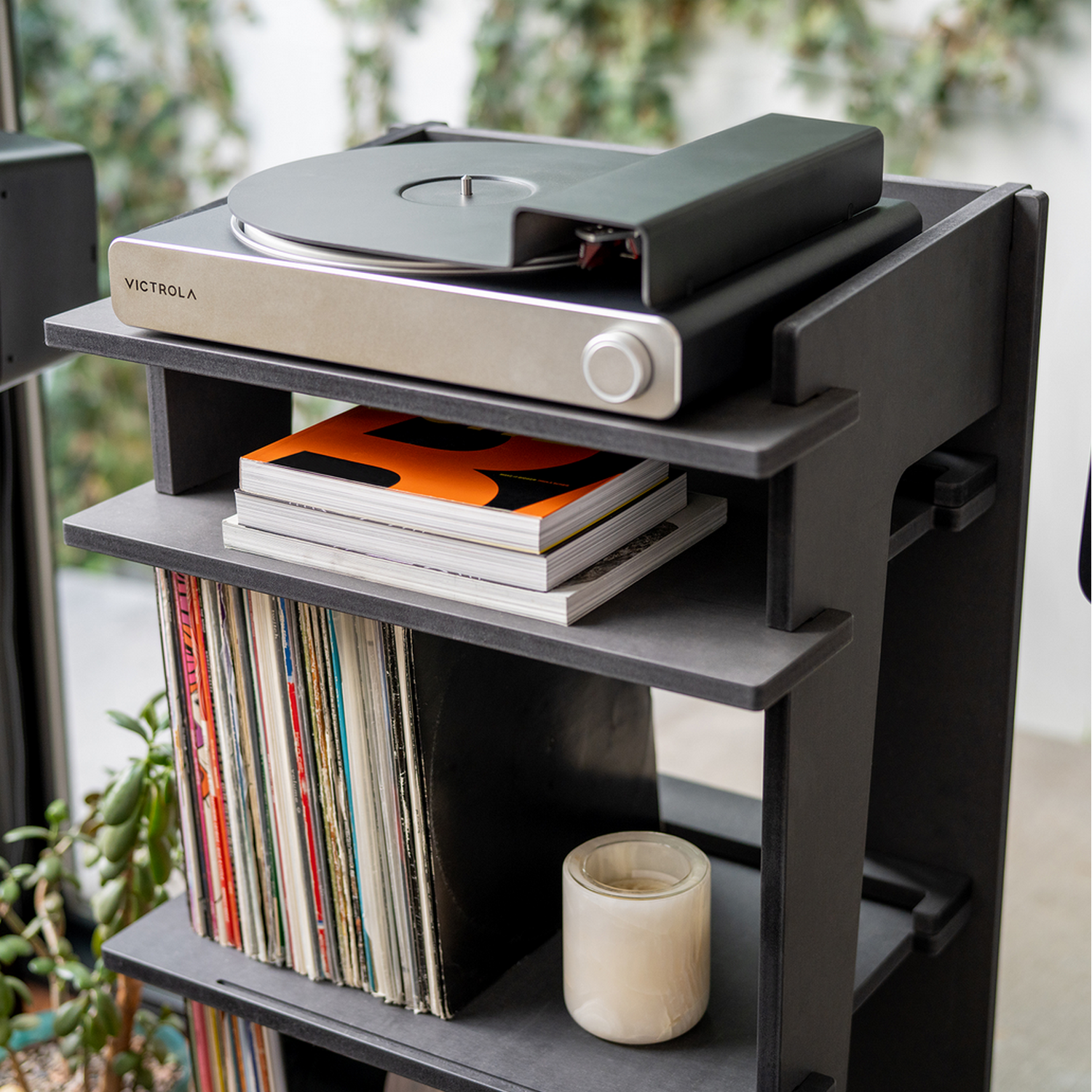 Een platenspeler op een zwarte plank met platen en boeken. Er staat een kaars op de plank.