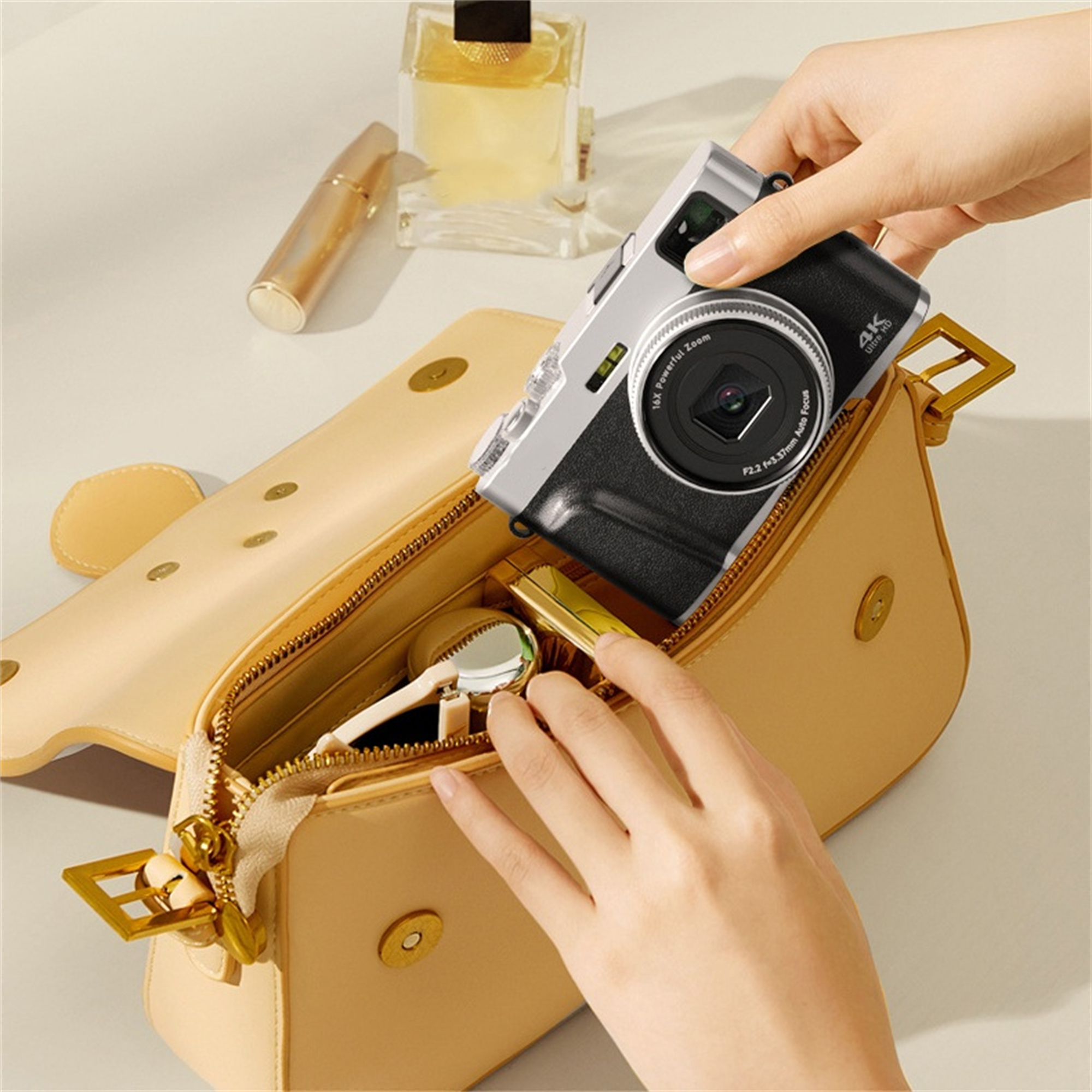 Hände legen eine silberne Kamera in eine beige Handtasche, mit anderen Gegenständen.