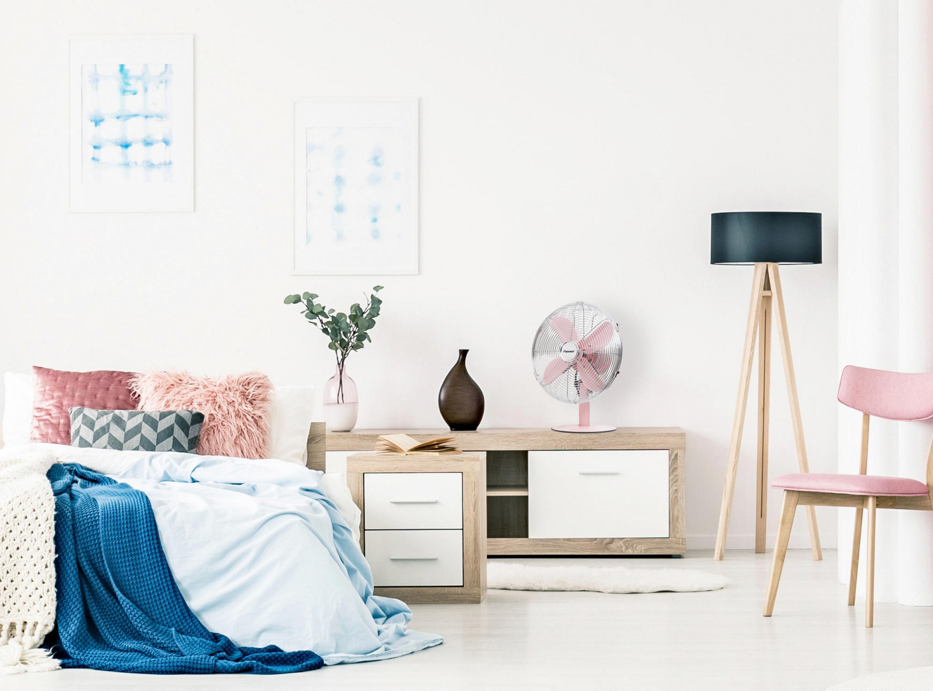 Scena della camera da letto: letto con coperta blu, cuscini rosa, ventilatore, mobili in legno e sedia rosa.