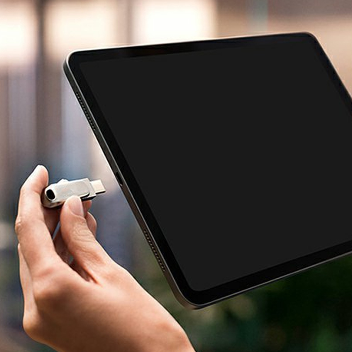 Hand hält einen silbernen USB-C-Stick neben einem schwarzen Tablet. Der Bildschirm des Tablets ist leer. Weißer Hintergrund.