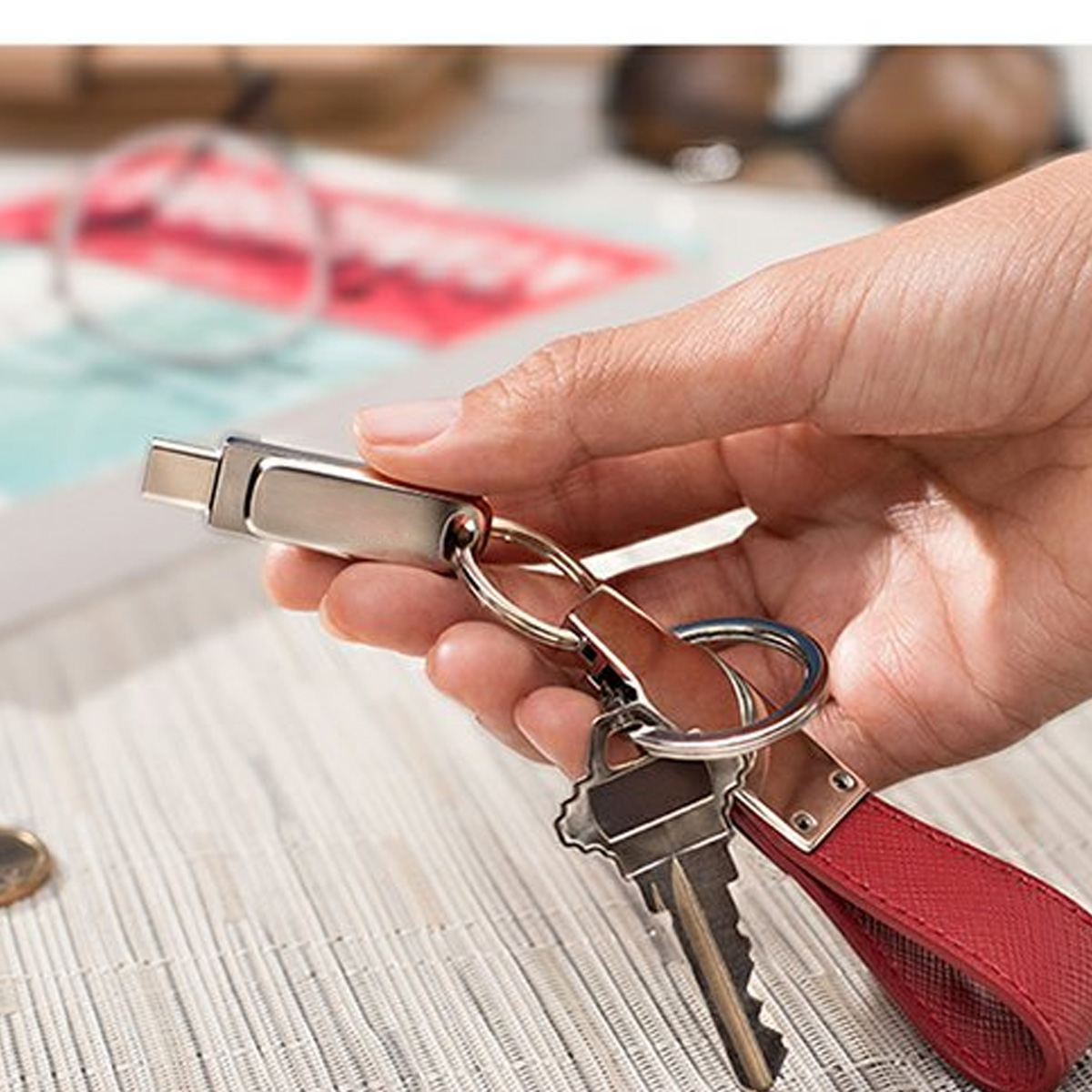Hand hält einen Schlüsselanhänger mit Schlüsseln und einem USB-C-Adapter auf hellfarbiger Oberfläche.