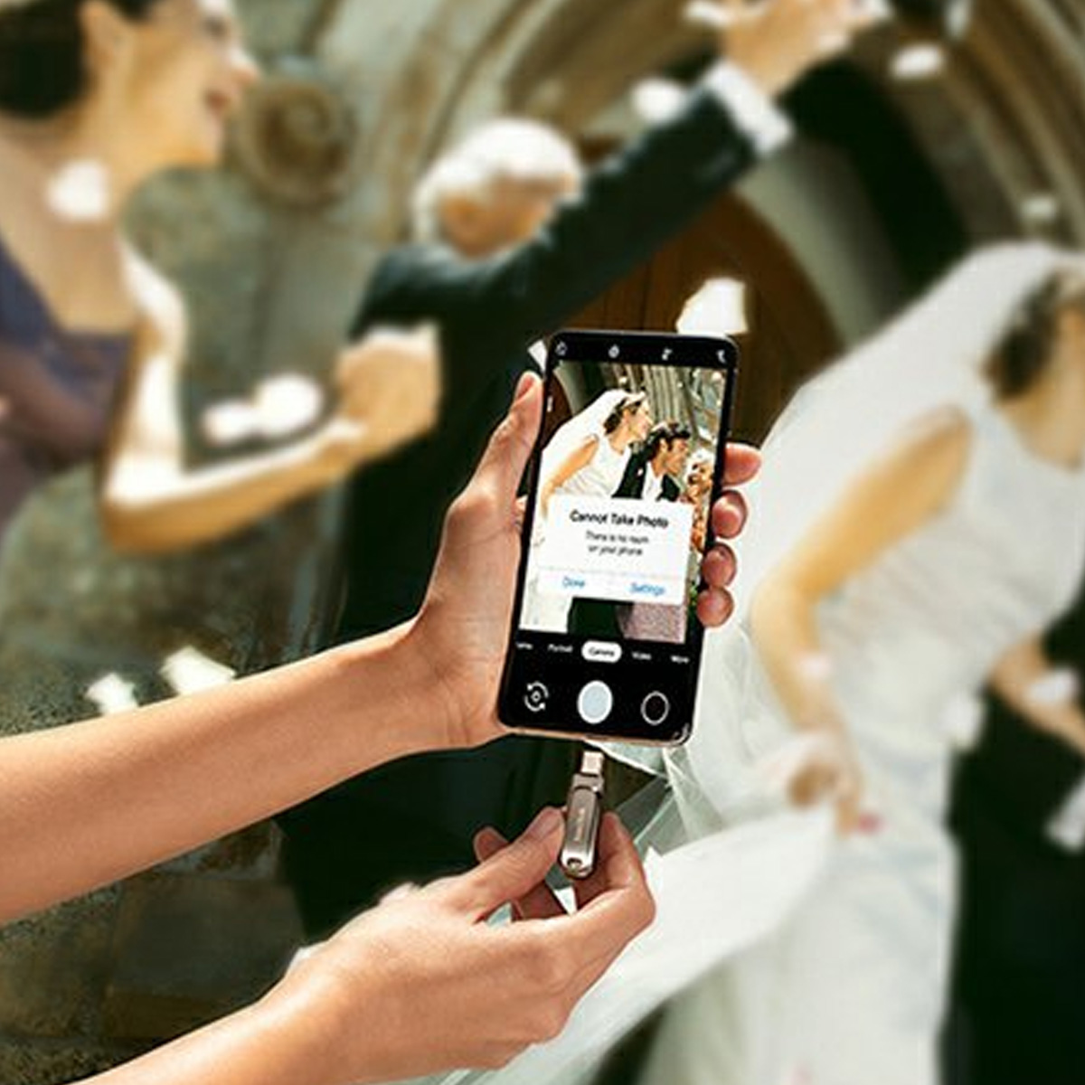 Eine Person hält ein Telefon und macht ein Foto auf einer Hochzeit. Andere Personen sind im Hintergrund unscharf.