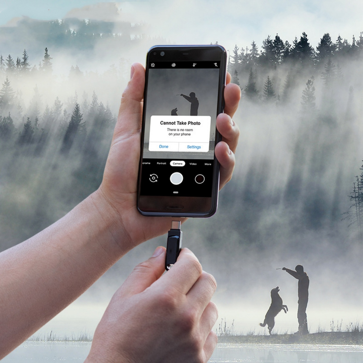 Ein Telefon zeigt „Foto kann nicht aufgenommen werden“. Eine Person hält es. Silhouetten von Personen und einem Hund spielen im Hintergrund.