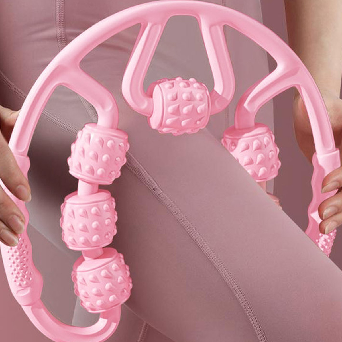 Ein rosa Rollenmassagegerät wird von zwei Händen gehalten. Der Hintergrund zeigt pinkfarbene Leggings.