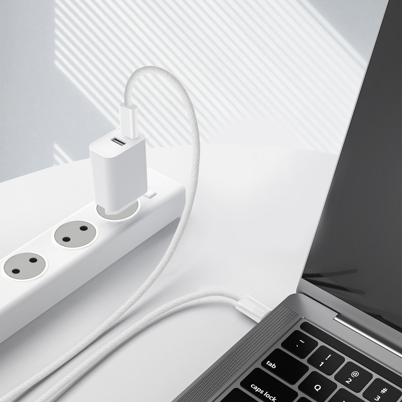 Een laptop wordt opgeladen via een witte kabel uit een stopcontact op een wit oppervlak.