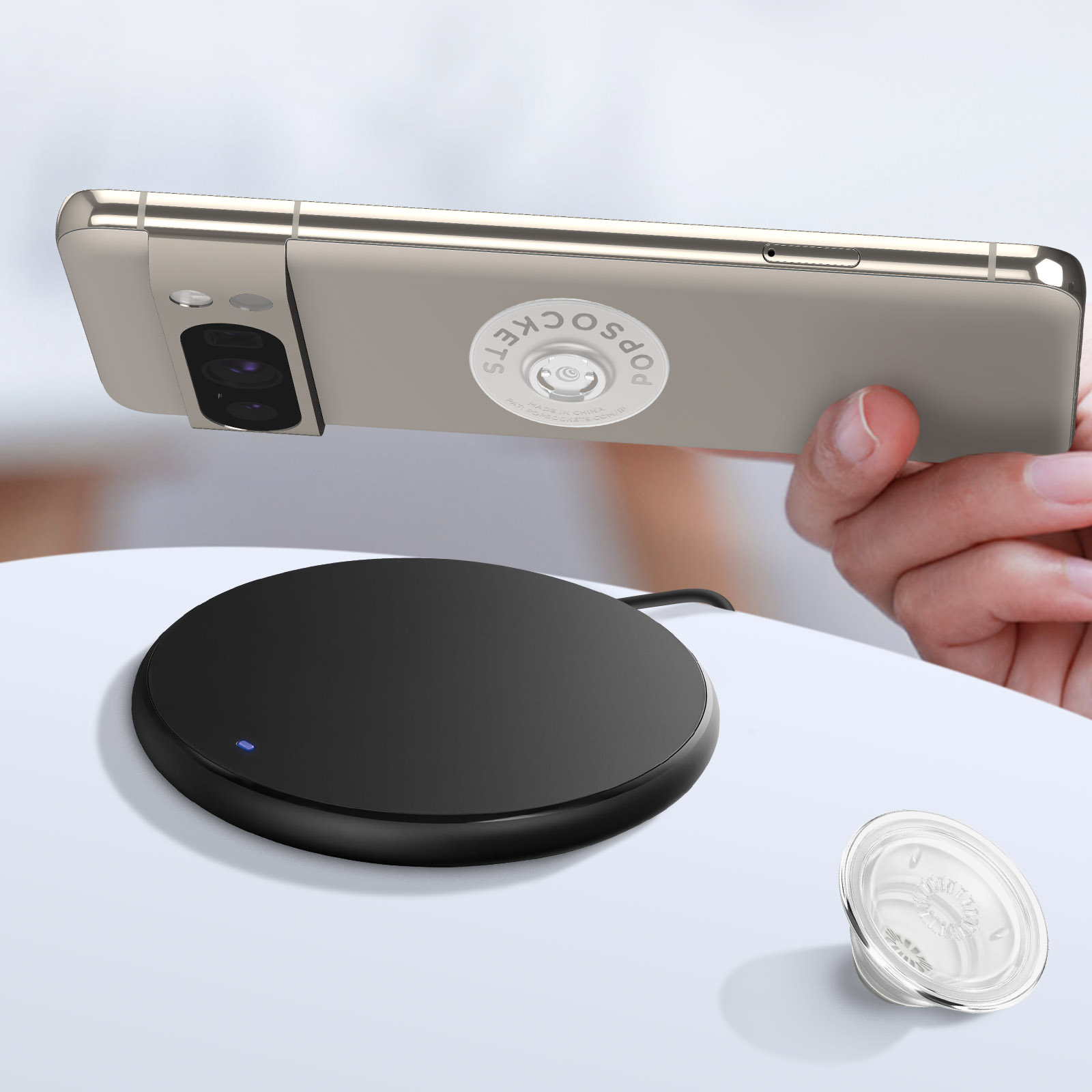 Ein Telefon mit Pop-Socket auf einem kabellosen Ladegerät. Ein durchsichtiger Pop-Socket befindet sich unten rechts.