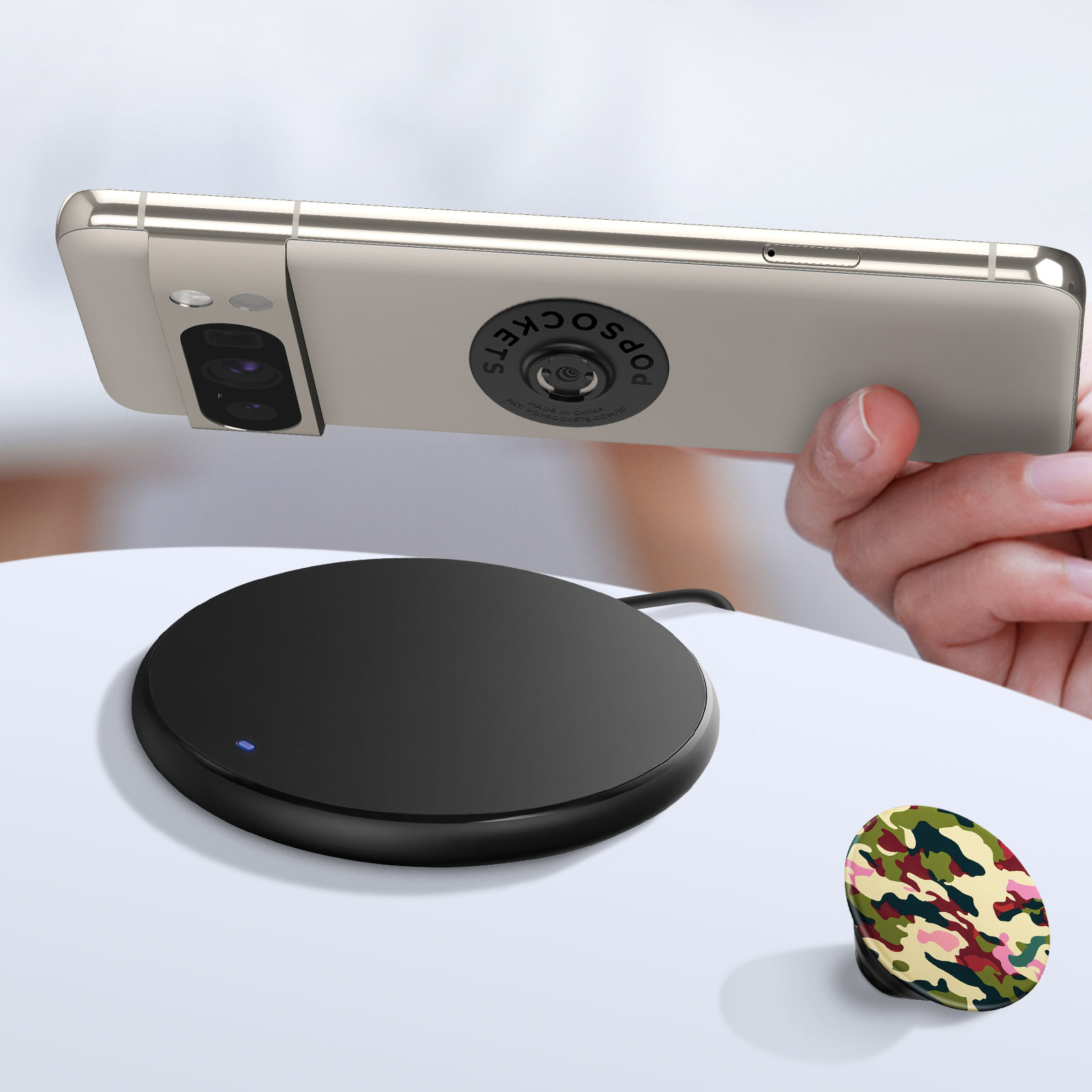 Ein Telefon mit Popsocket auf einem kabellosen Ladegerät und ein Camo-Popsocket.