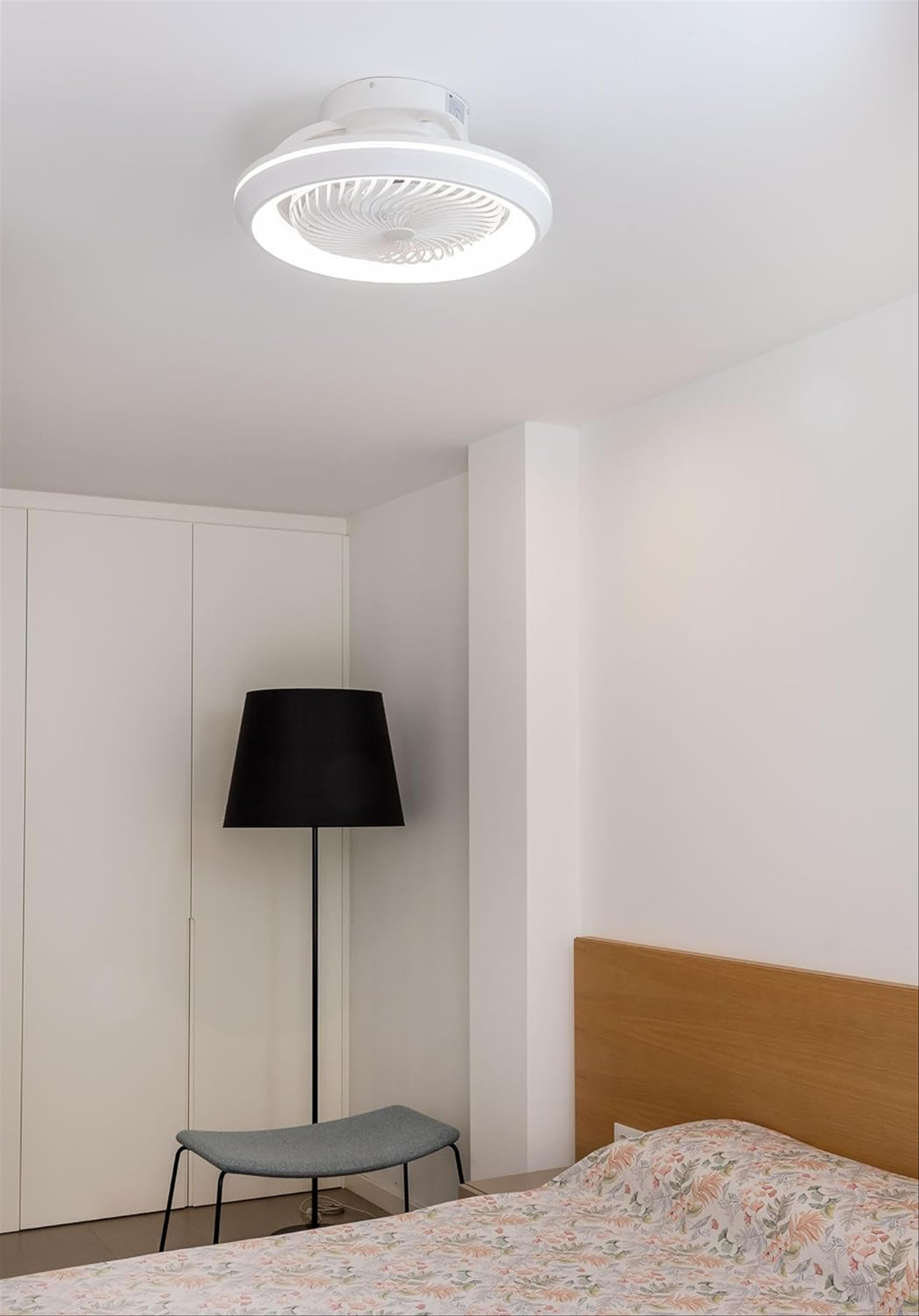 Interior de dormitorio. Ventilador de techo con luz. Lámpara de pie negra. Cama con manta floral.
